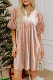 A woman wearing a dusty pink velvet mini dress with short lace puff sleeves, standing in front of a decorated Christmas tree.
