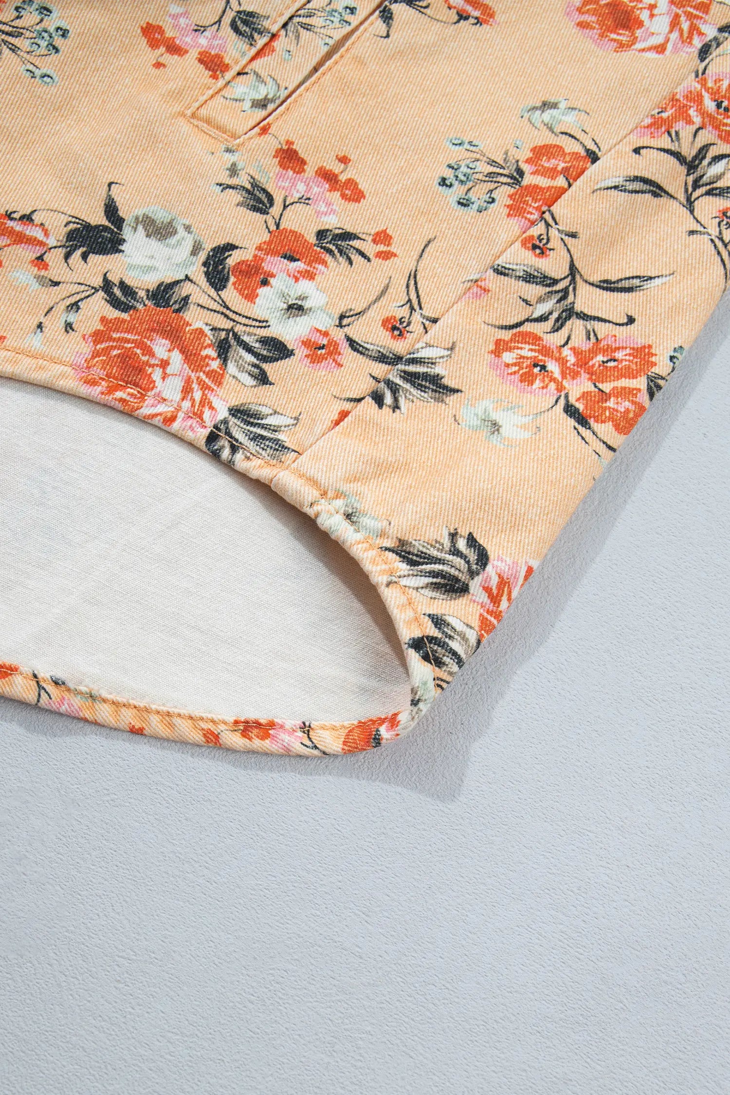 Close-up of peach floral garment with orange, white, and black flowers and white lining along curved hem.