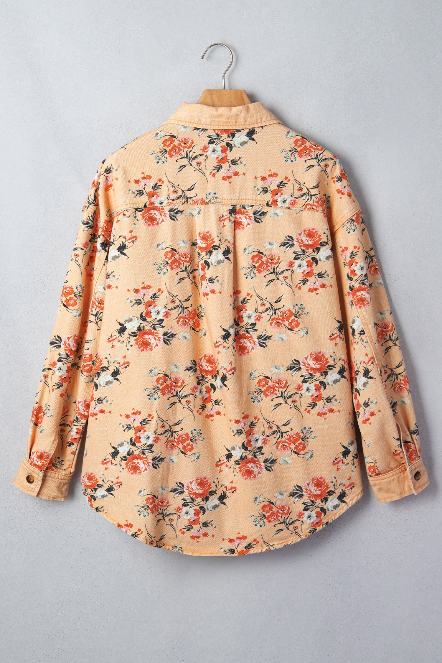 Peach-beige floral button-up shirt with orange, red and green print hanging on a wooden hanger.