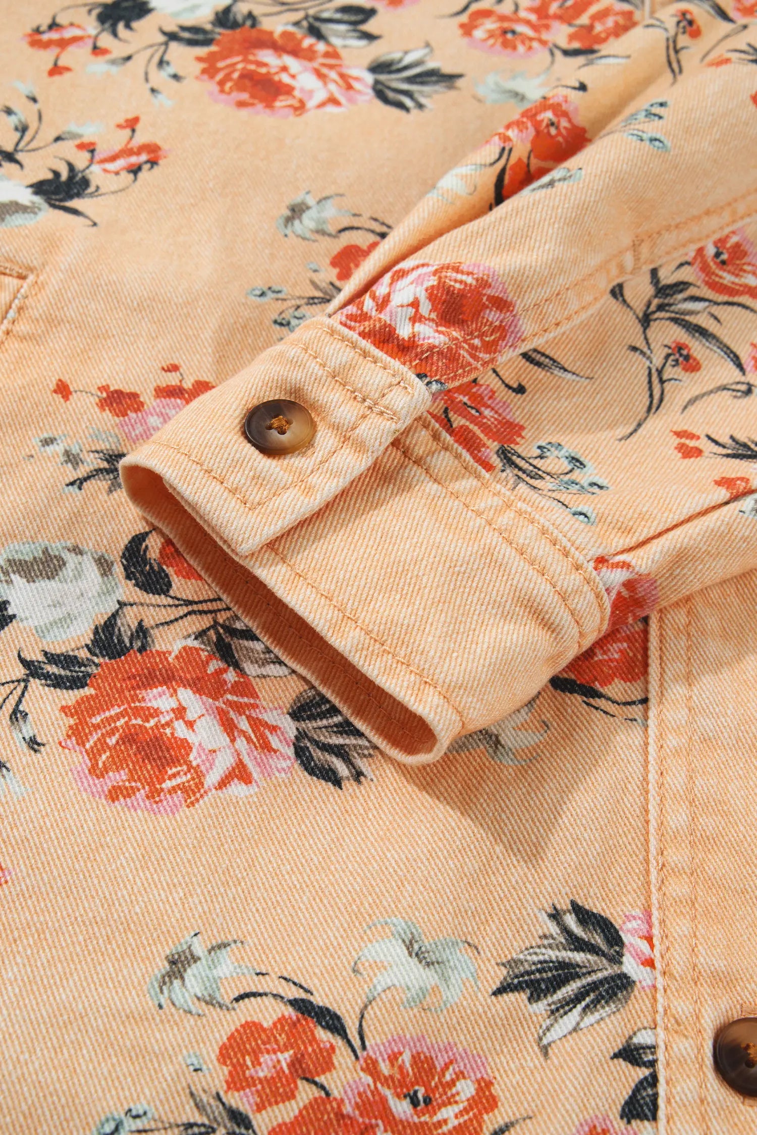 Close-up of peach denim jacket with orange, pink, and black floral print and buttoned cuff detail.