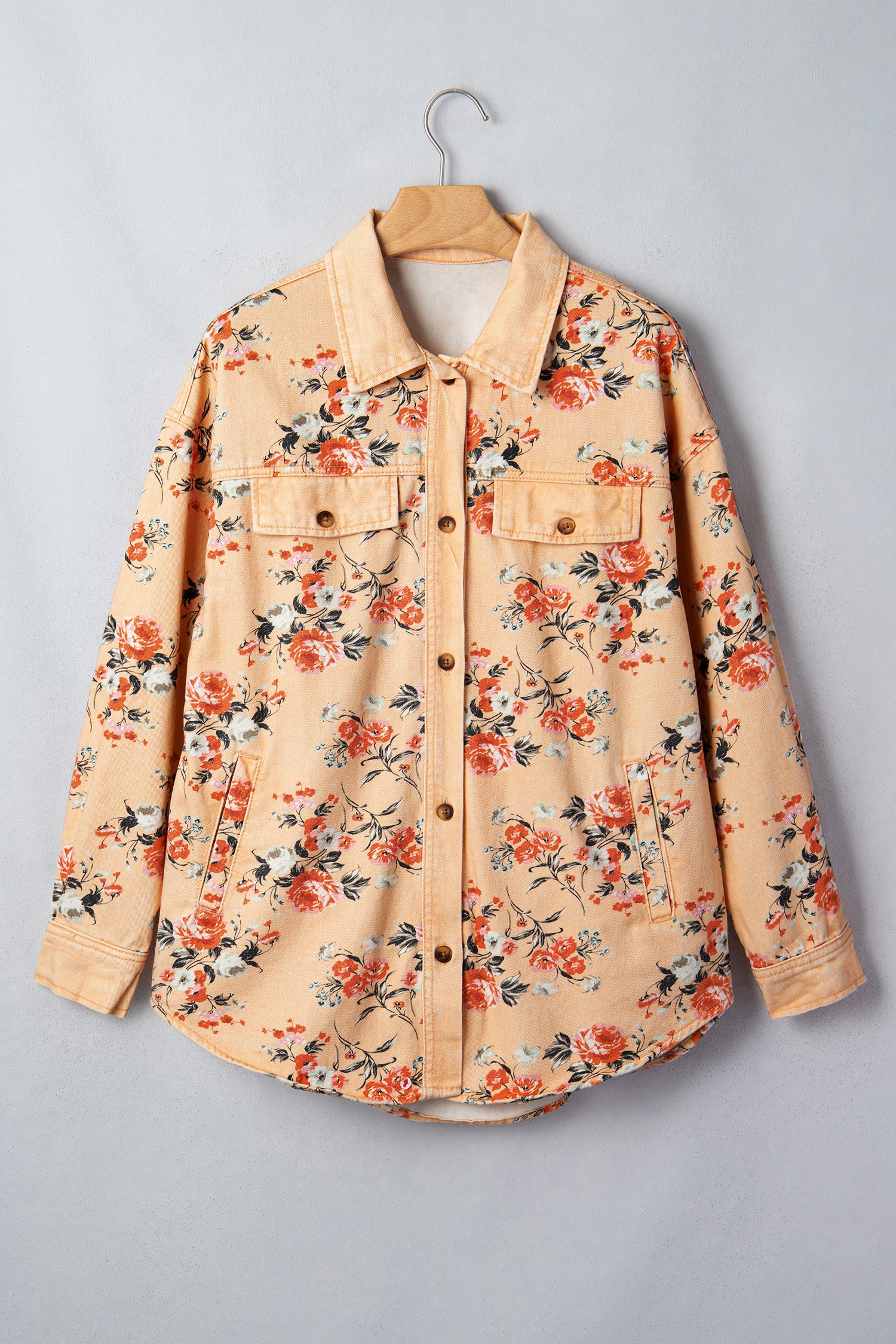 Light beige floral denim shirt jacket with orange, red and green leaf print on wooden hanger.