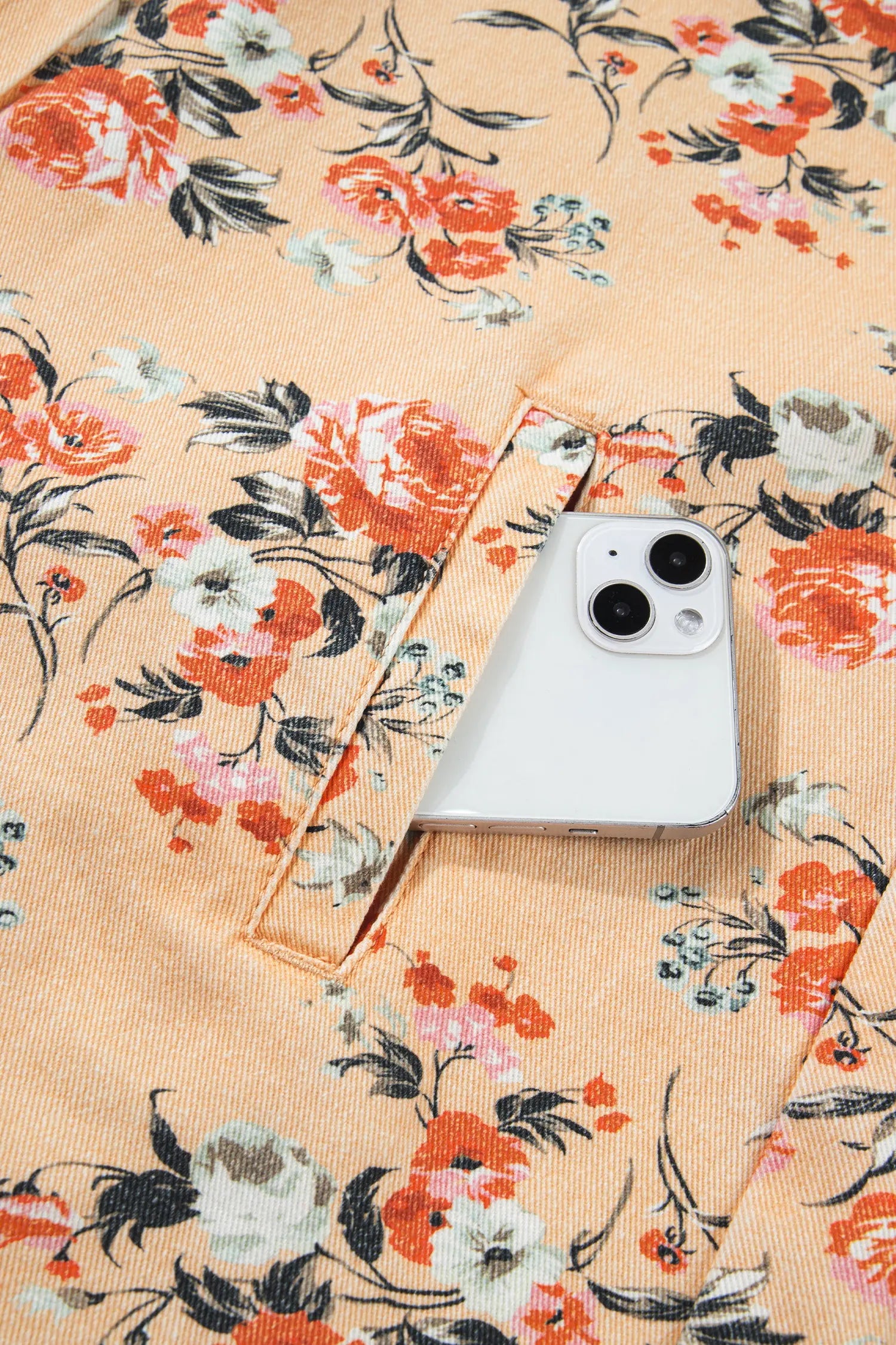 Close-up of peach fabric with orange, white, and black floral print and stitched pocket holding a smartphone.