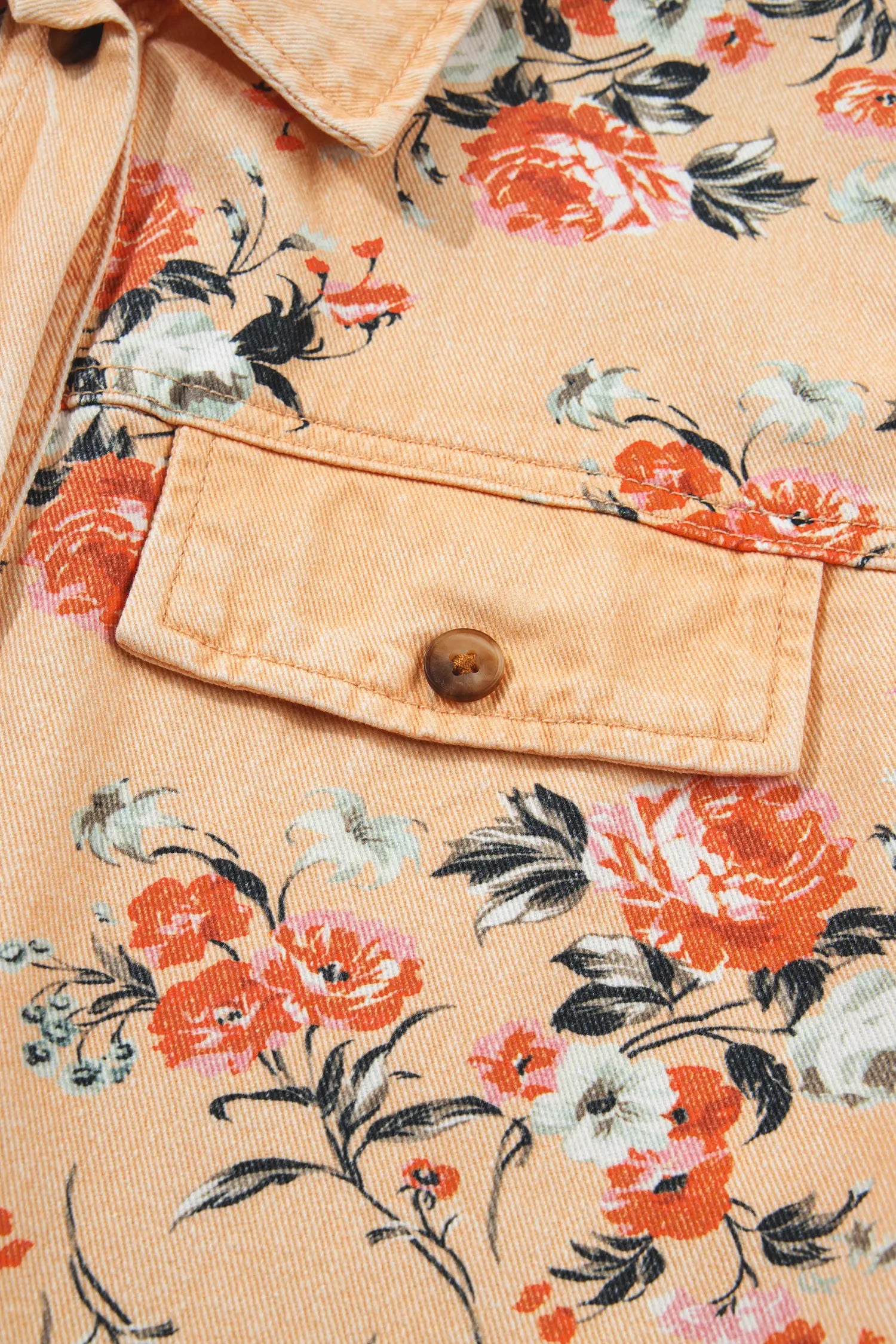 Close-up of peach shirt jacket with vibrant orange, white, and black floral print and buttoned chest pocket.