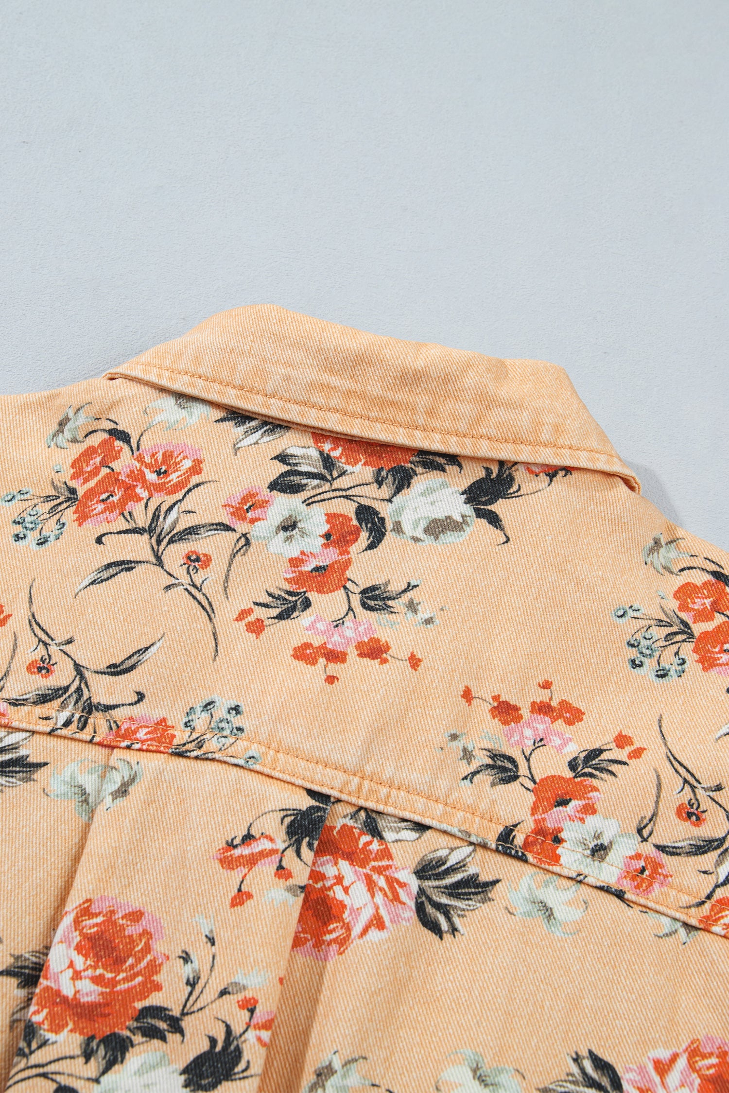 Close-up of light peach shirt with vibrant orange, red and white floral print and collar detail.