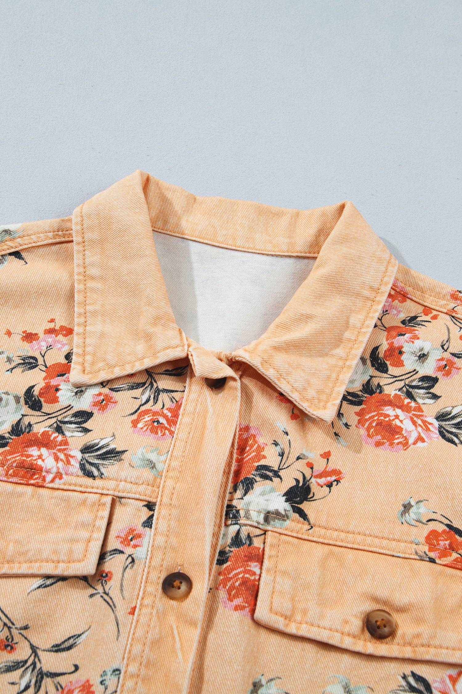 Close-up of light peach denim shirt jacket with orange, red, and black floral print and button front.