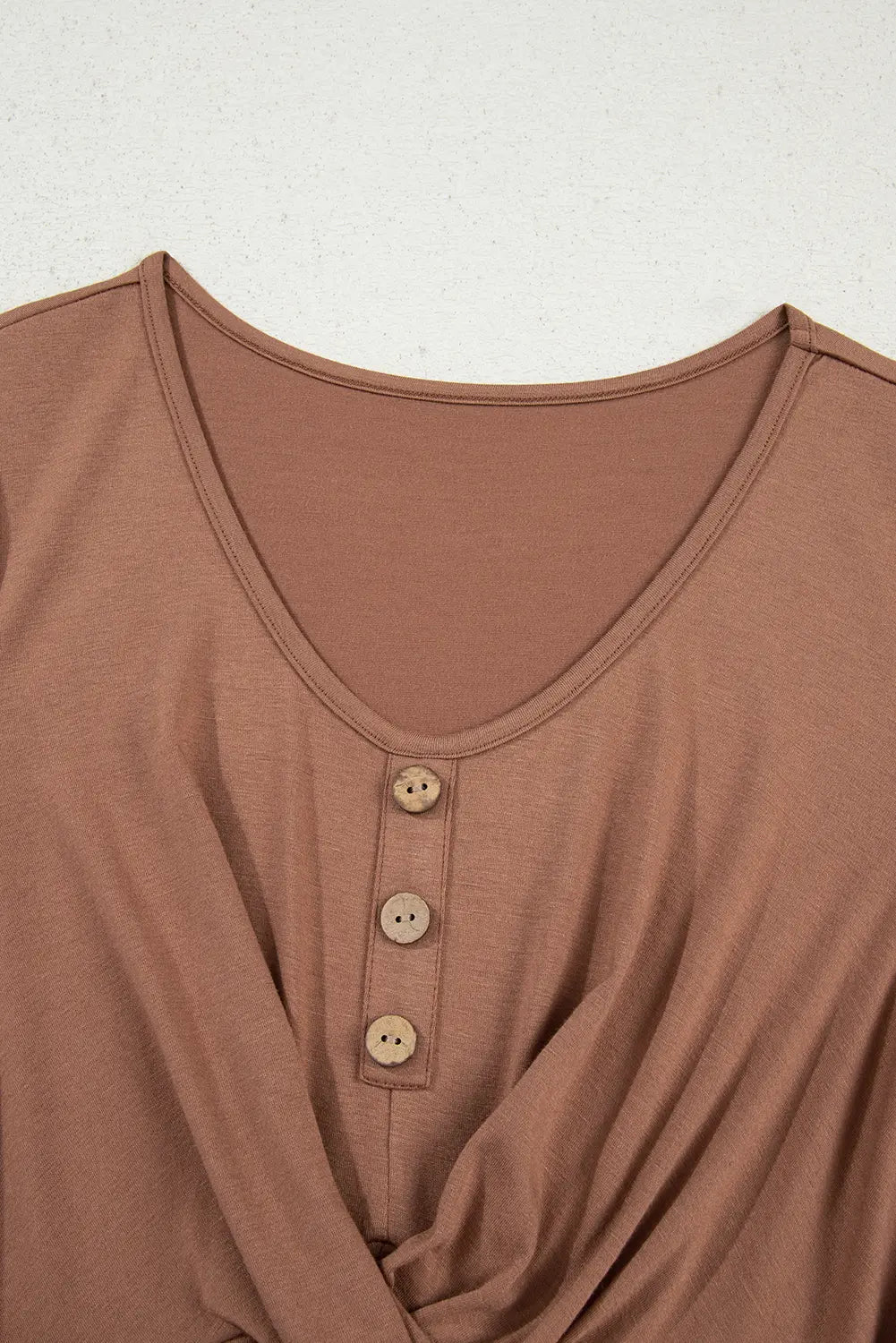 Close-up of a brown v-neck top with a three-button henley neckline, featuring a twisted front detail at the waist.
