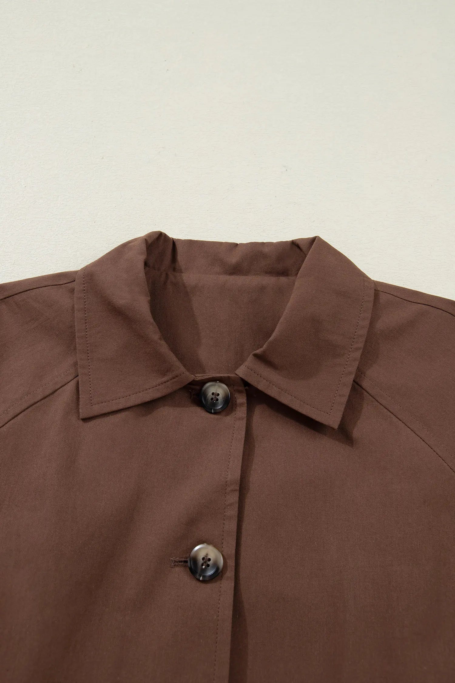 Close-up of a brown jacket collar and buttons on a beige background