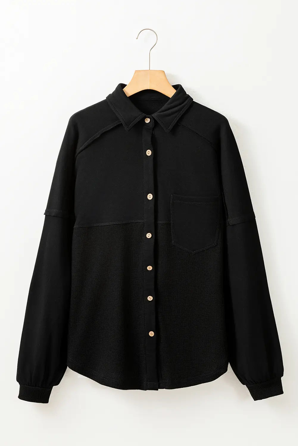 Black shirt with buttons on a wooden hanger against a white background