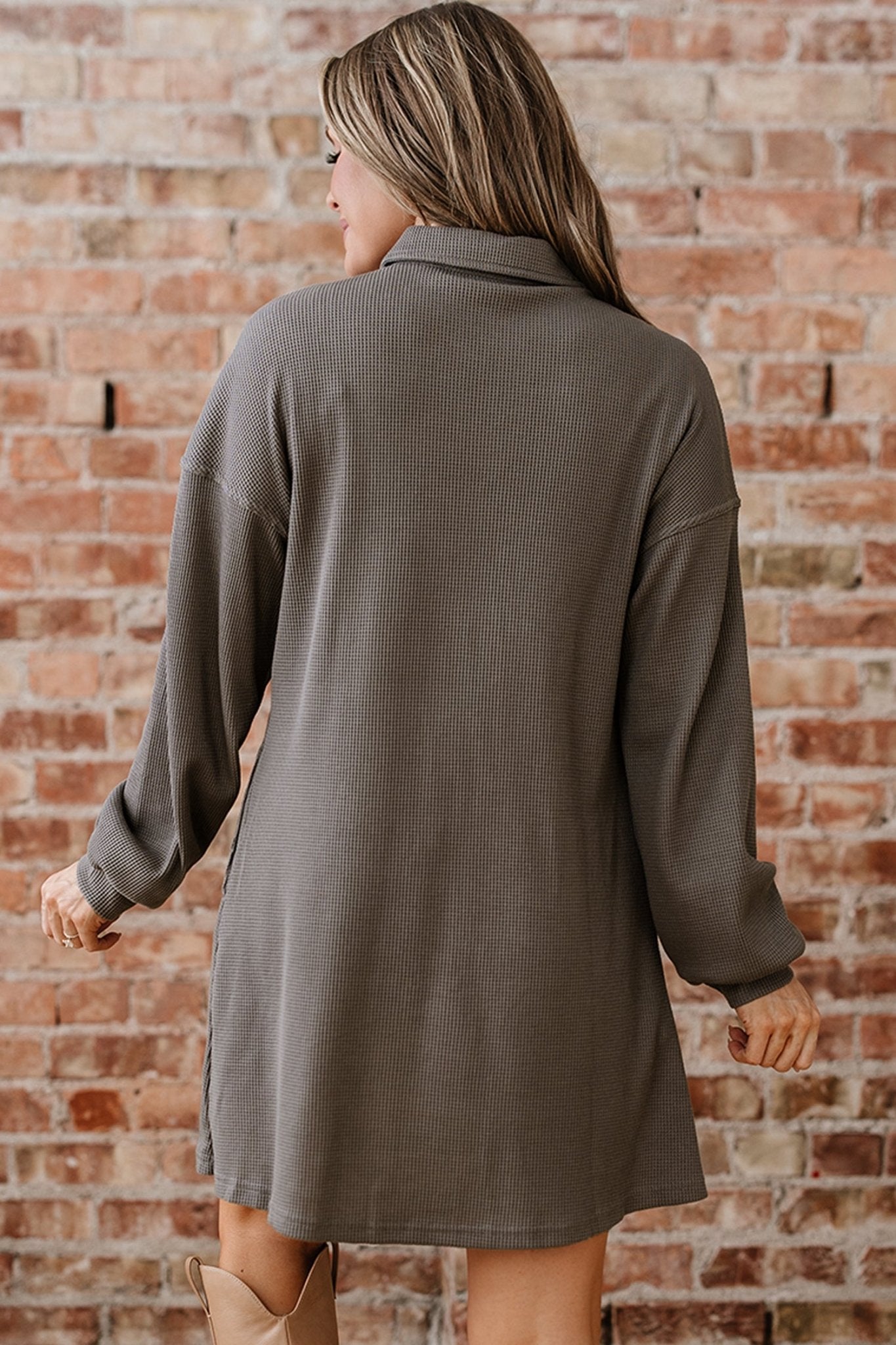 Woman wearing a gray coat against a brick wall