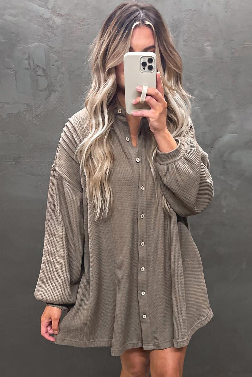 Woman taking a mirror selfie wearing a long-sleeve button-up dress against a gray background