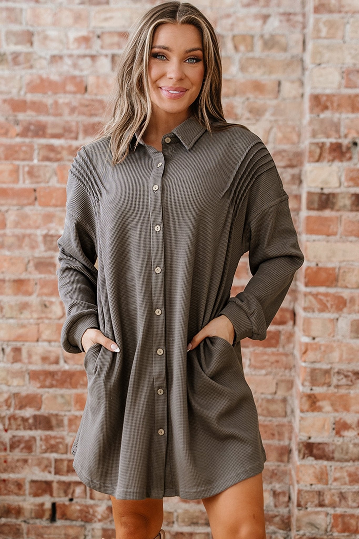 Woman wearing a gray button-up dress against a brick wall