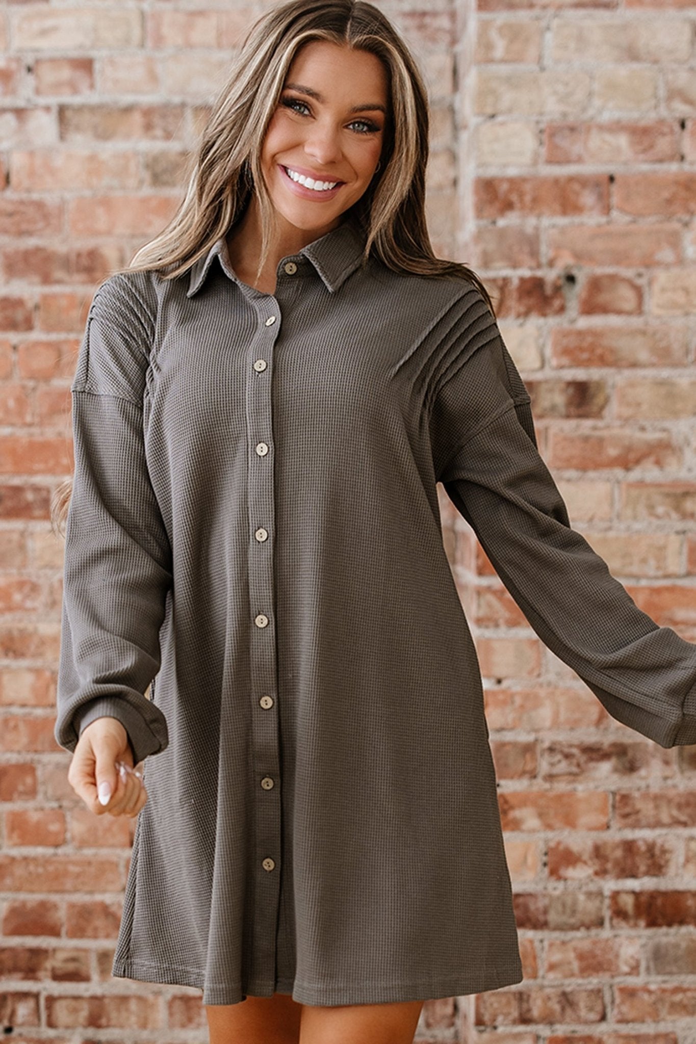 Woman wearing a gray button-up dress against a brick wall
