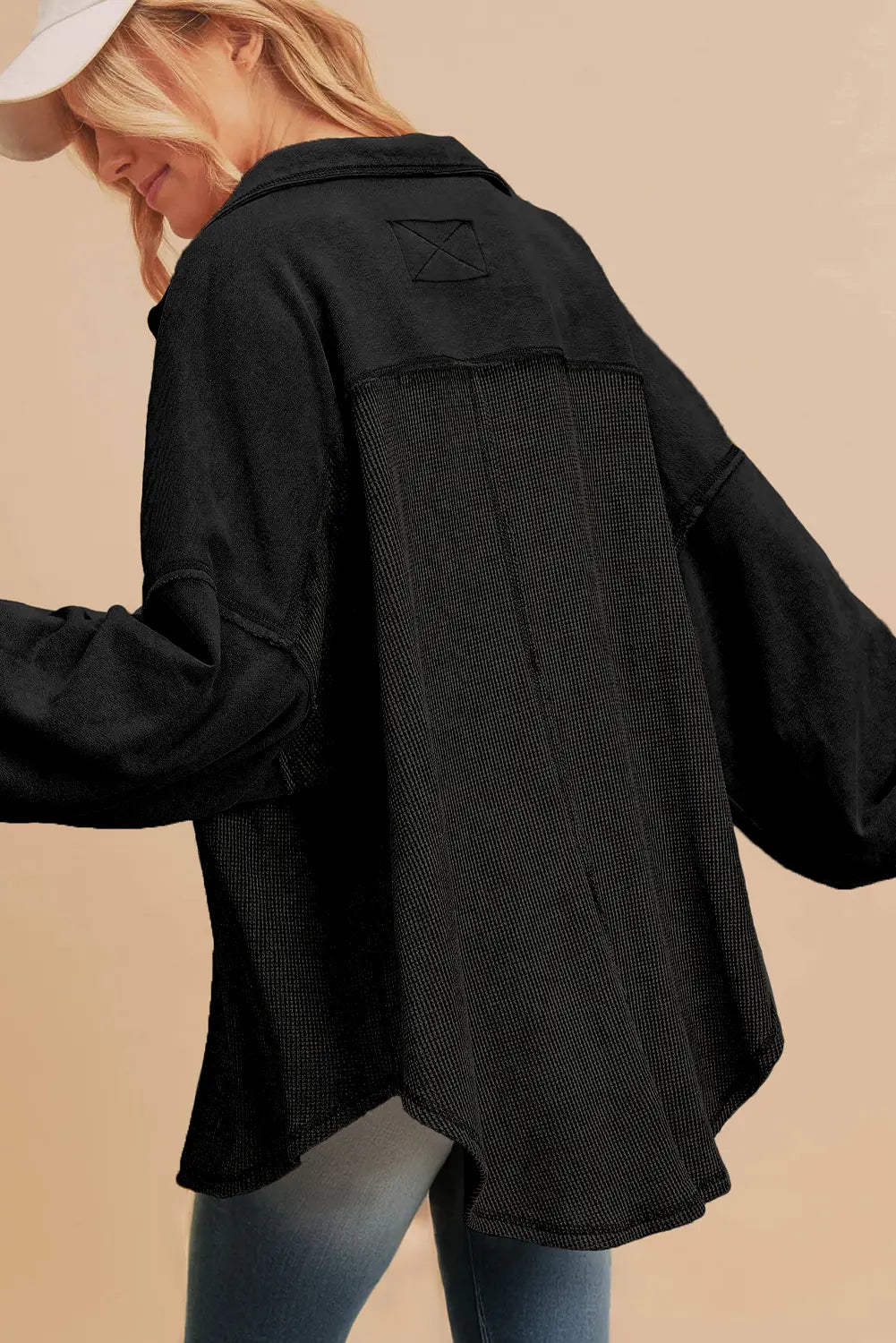 Person wearing a black jacket with a brand logo on a beige background