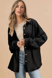 Woman wearing a black button-up shirt over a white top and blue jeans on a beige background