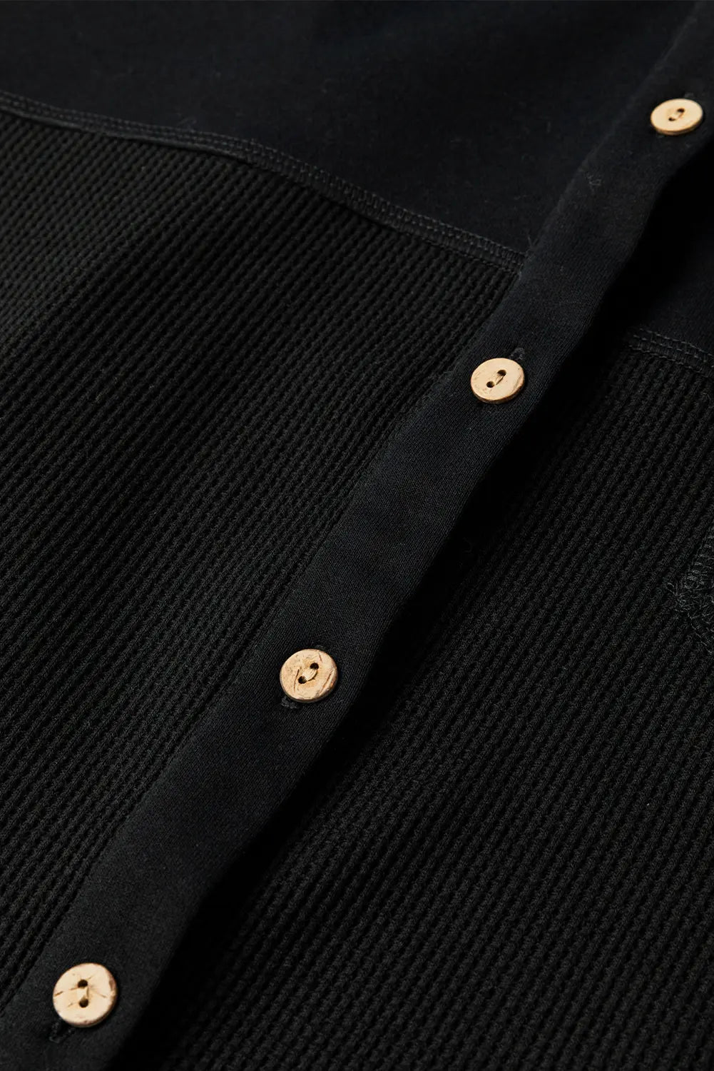Close-up of a black ribbed knit button-up shirt with light brown buttons, showing the texture and fabric details.