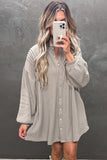 Woman taking a mirror selfie wearing a light gray button-up dress against a dark background