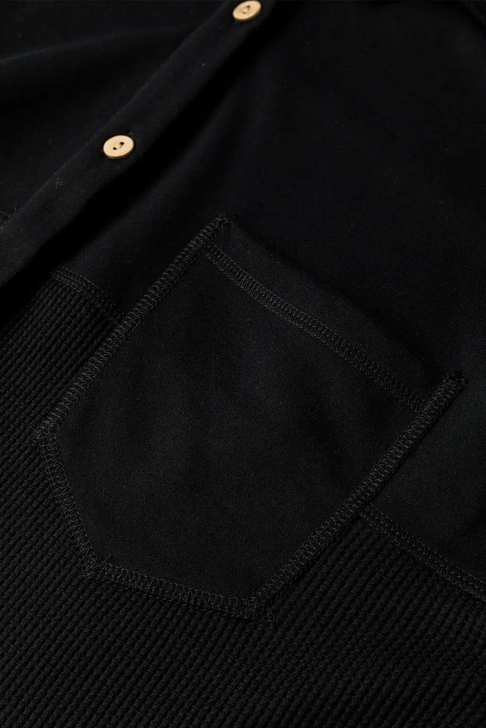 Close-up detail of a black textured knit button-up shirt with a solid black fabric chest pocket and small gold-tone buttons.