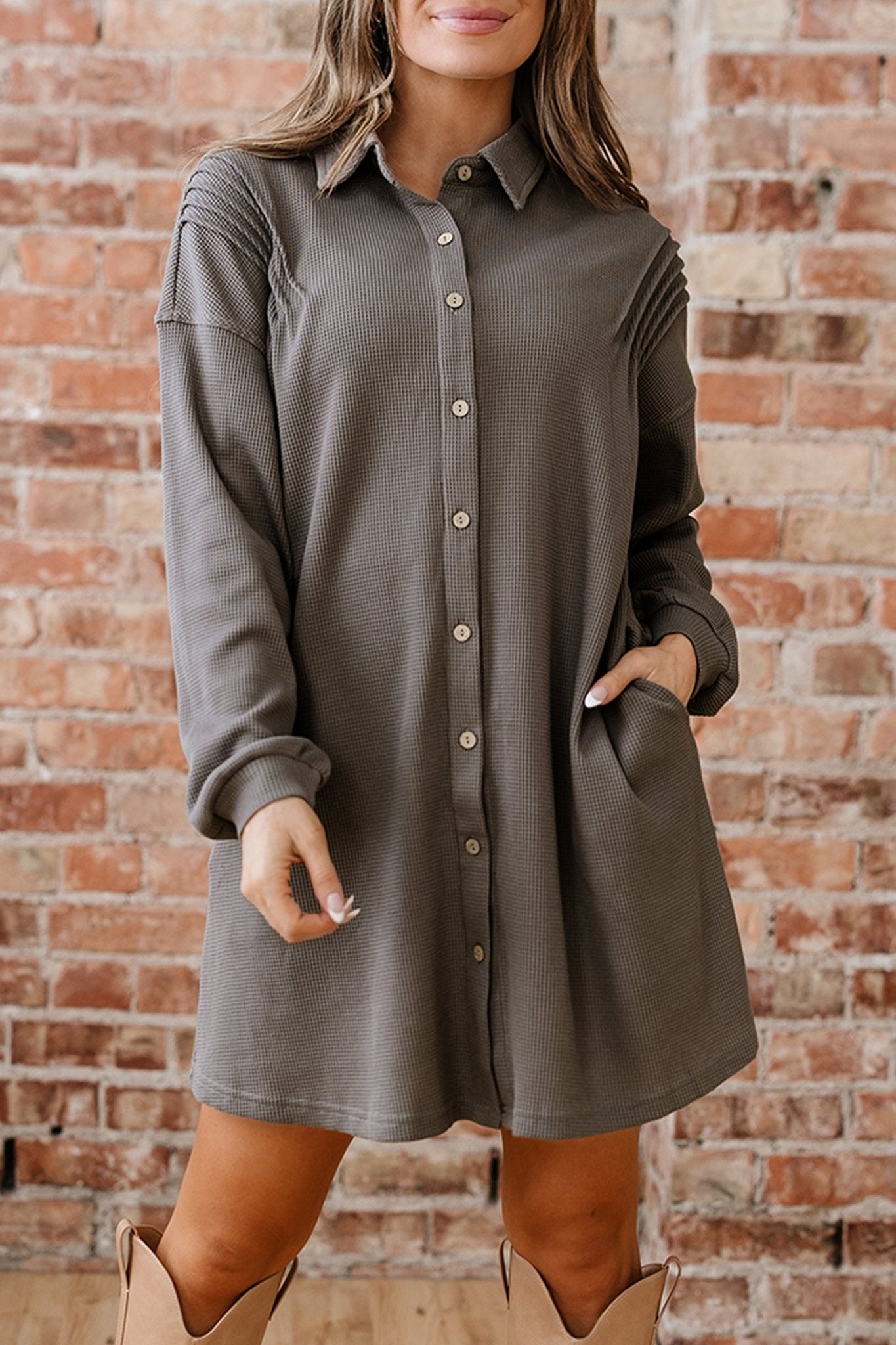 Person wearing a gray button-up dress against a brick wall