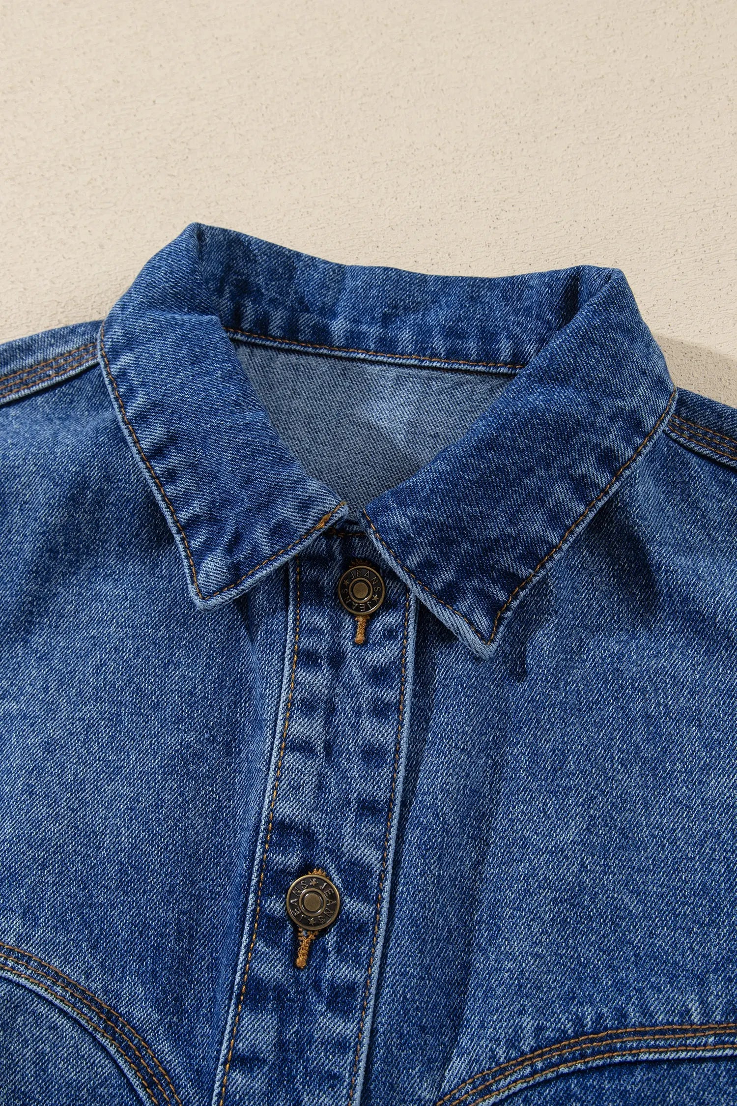 Close-up of blue denim shirt jacket with pointed collar, button placket, and contrast stitching.
