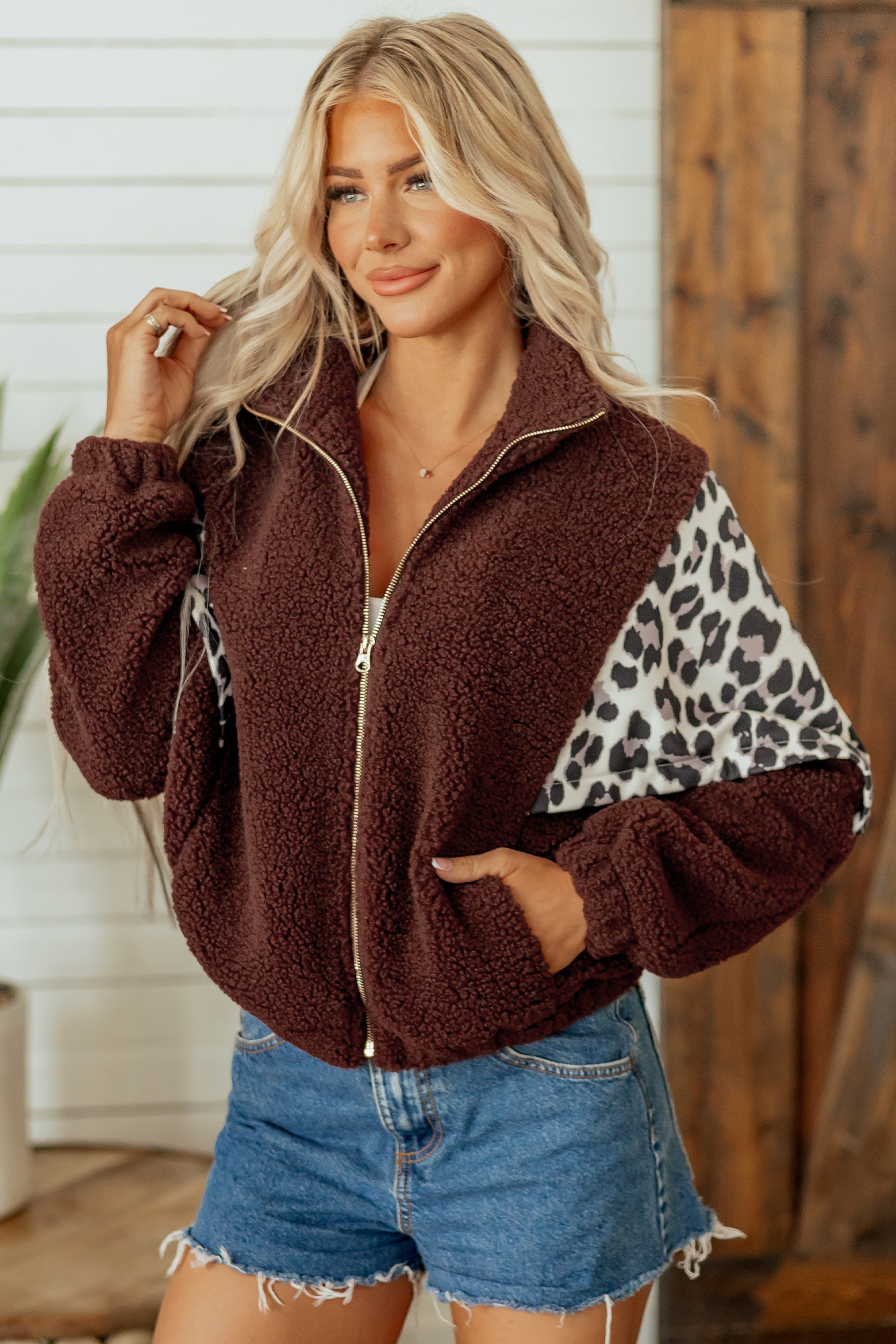 Woman in brown sherpa zip-up jacket with leopard-print panels and denim shorts.