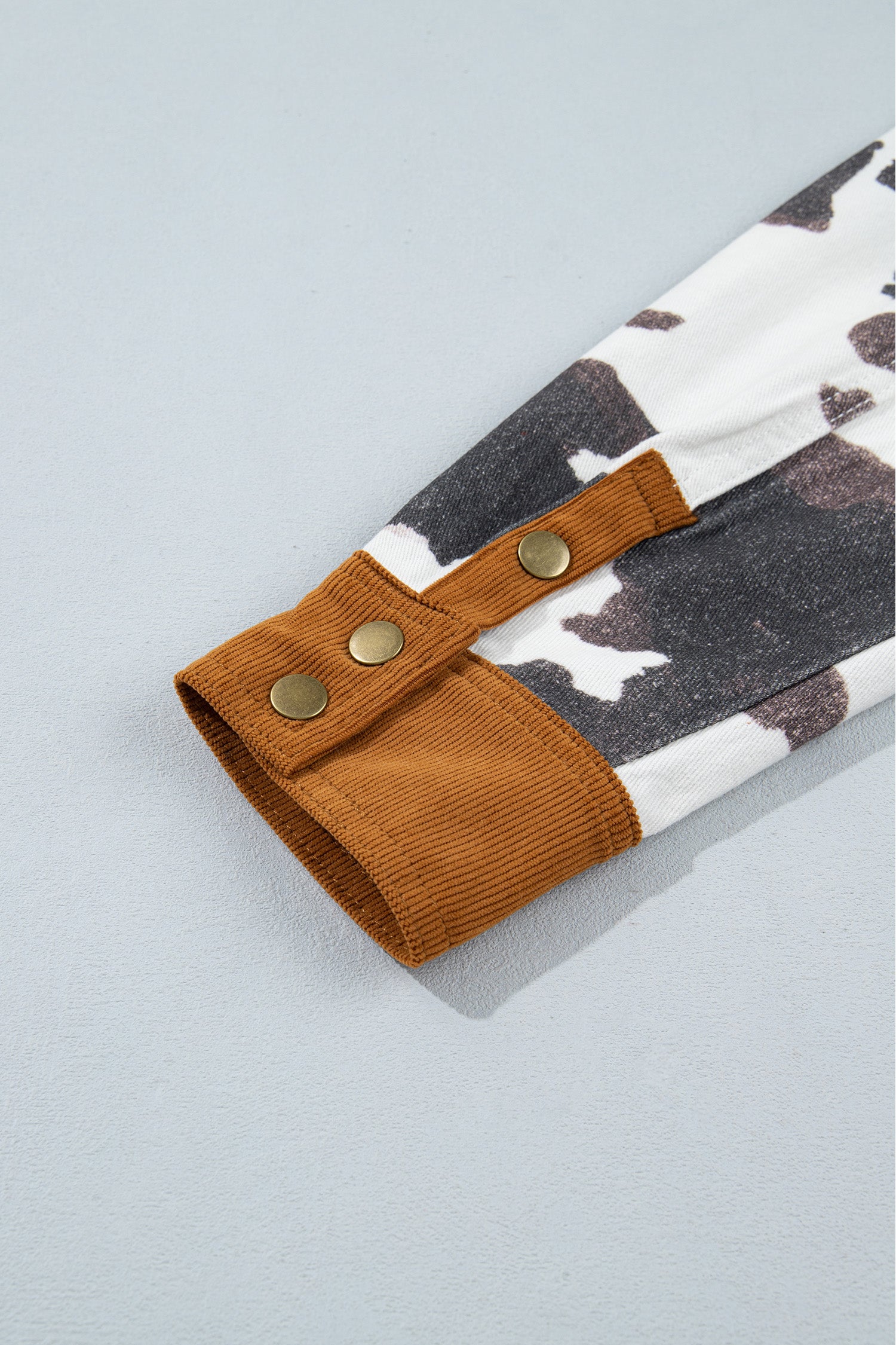 Close-up of children's cow-print sleeve with brown ribbed cuff and three brass snap buttons.