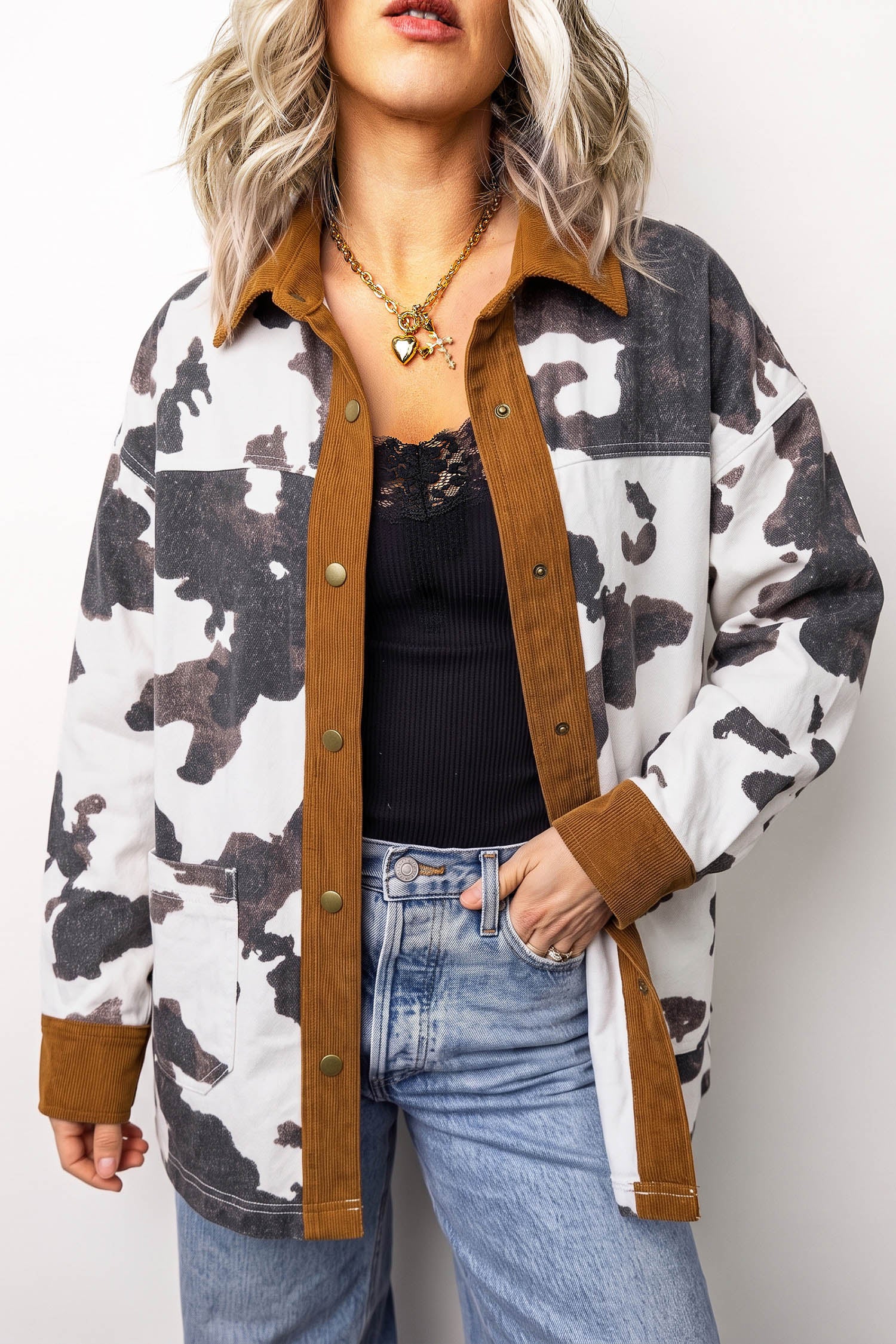 Woman wearing brown and black cow-print shirt jacket with suede-like trim over black top and blue jeans.