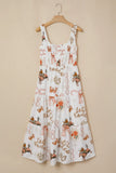 A white sleeveless sundress with a smocked bodice and tiered skirt, featuring an all-over whimsical print of fairies, bows, and autumn motifs in orange, brown, and beige, hanging on a wooden hanger against a solid beige wall.