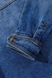 Close-up of blue denim garment with folded cuff, button tab, orange stitching