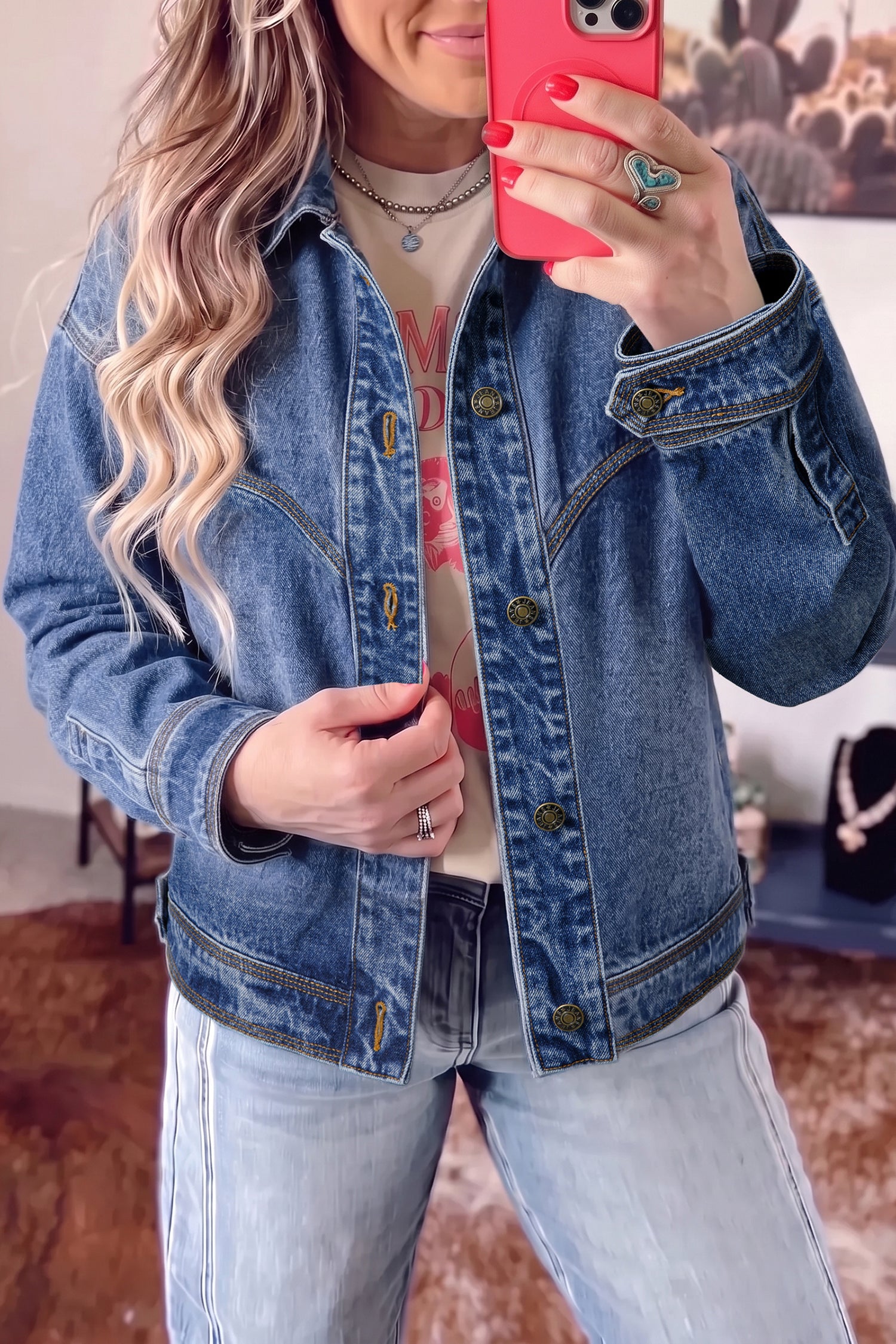 Woman taking a mirror selfie in a blue denim jacket, graphic T-shirt, and light-wash jeans