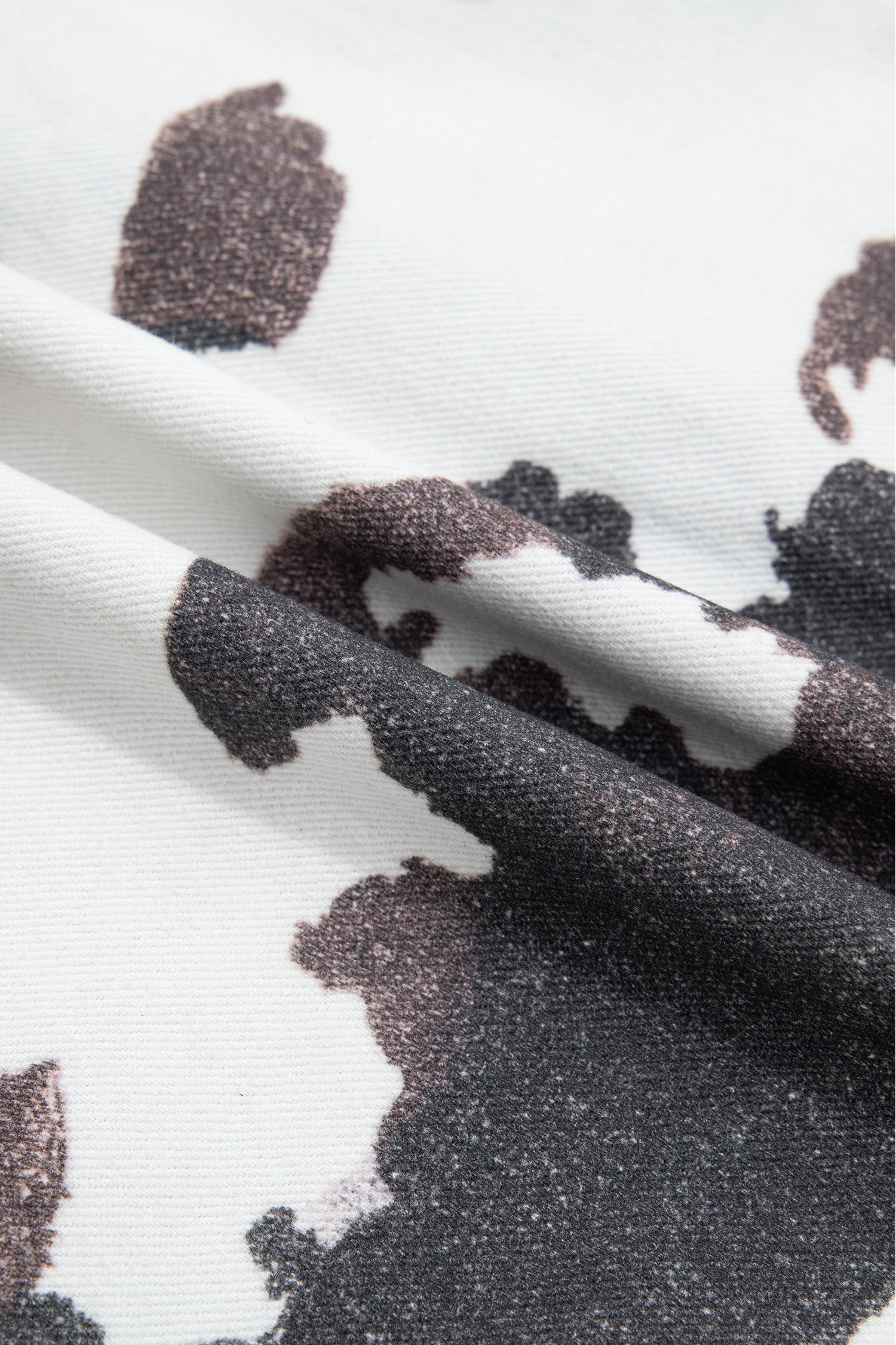 Close-up of white knit fabric with black and dark brown cow-print pattern