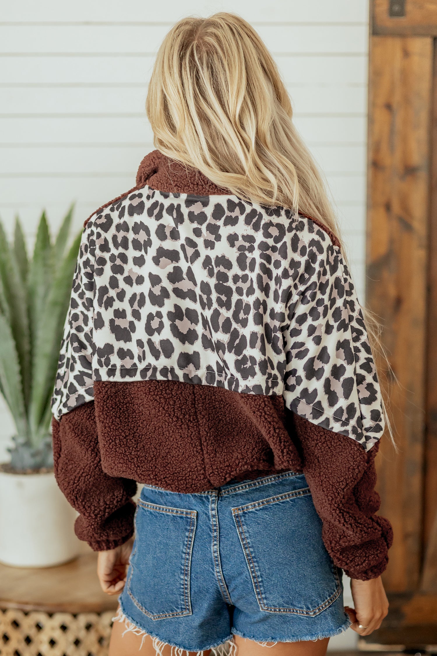 Back view of woman in brown leopard-print fleece jacket with denim shorts.