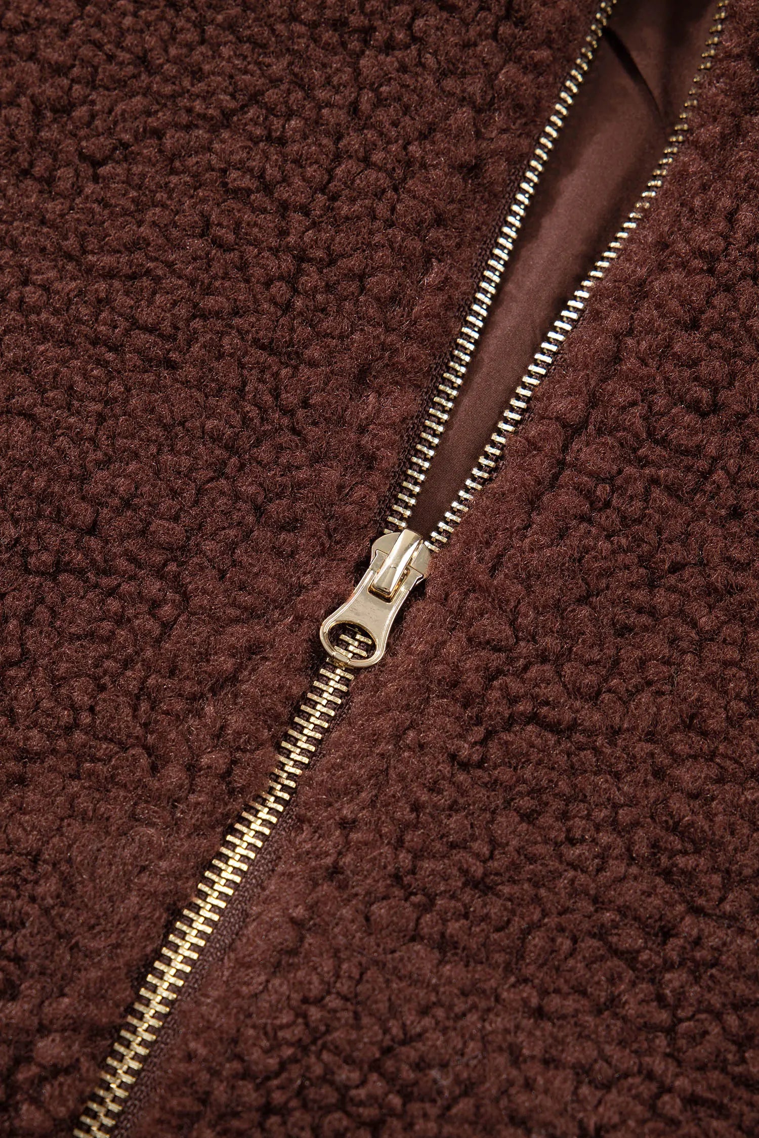 Close-up of a brown sherpa fleece jacket with a gold-tone metal zipper.