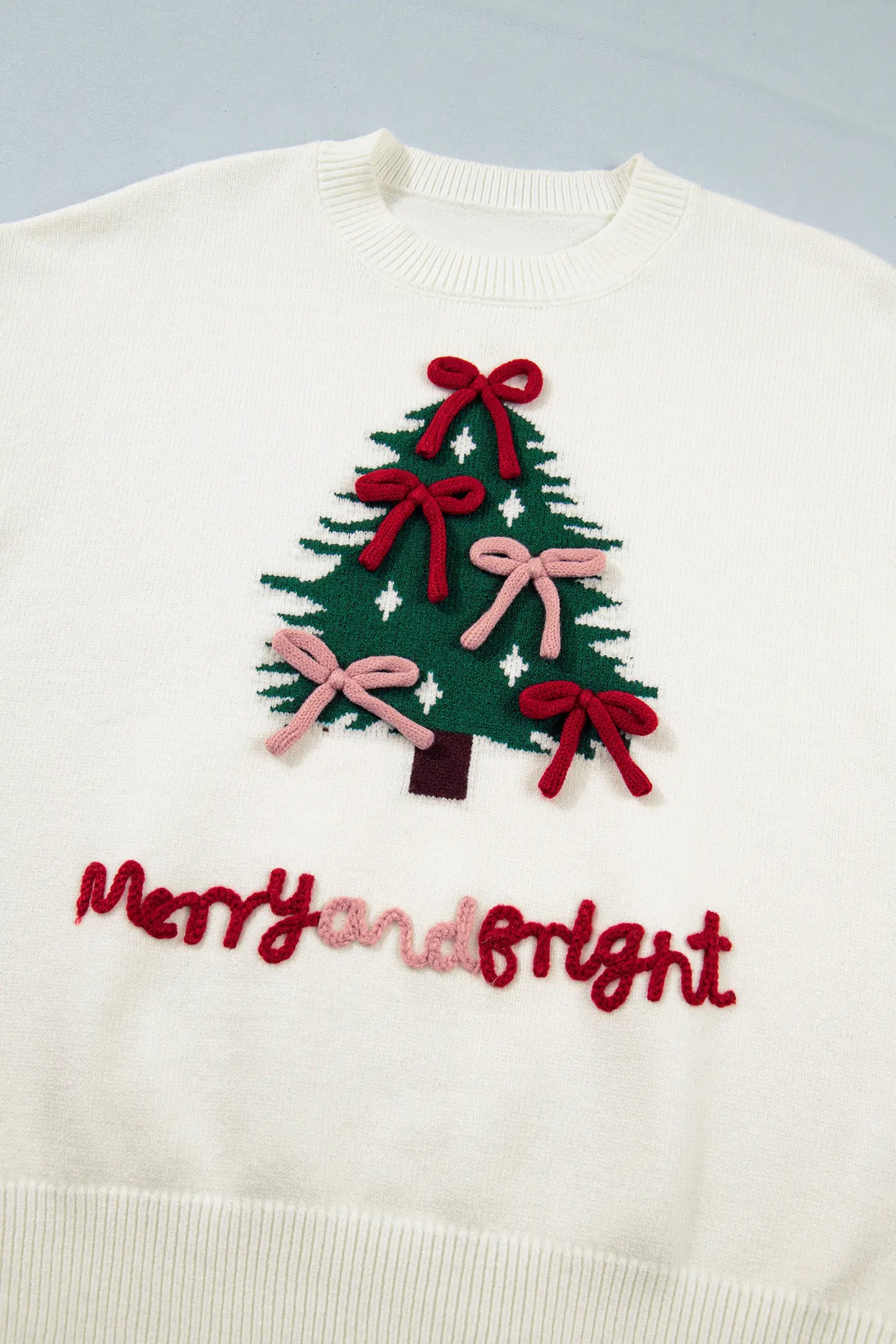 Off-white knit sweater with a green Christmas tree, colorful bows, and “Merry and Bright” lettering.
