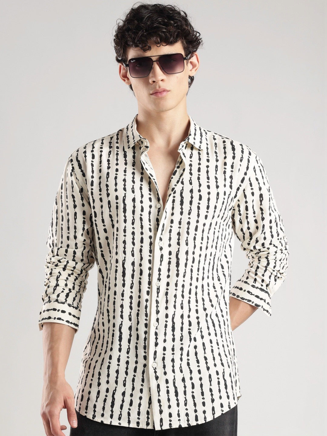 Man wearing a black and white patterned shirt with sunglasses on a gray background
