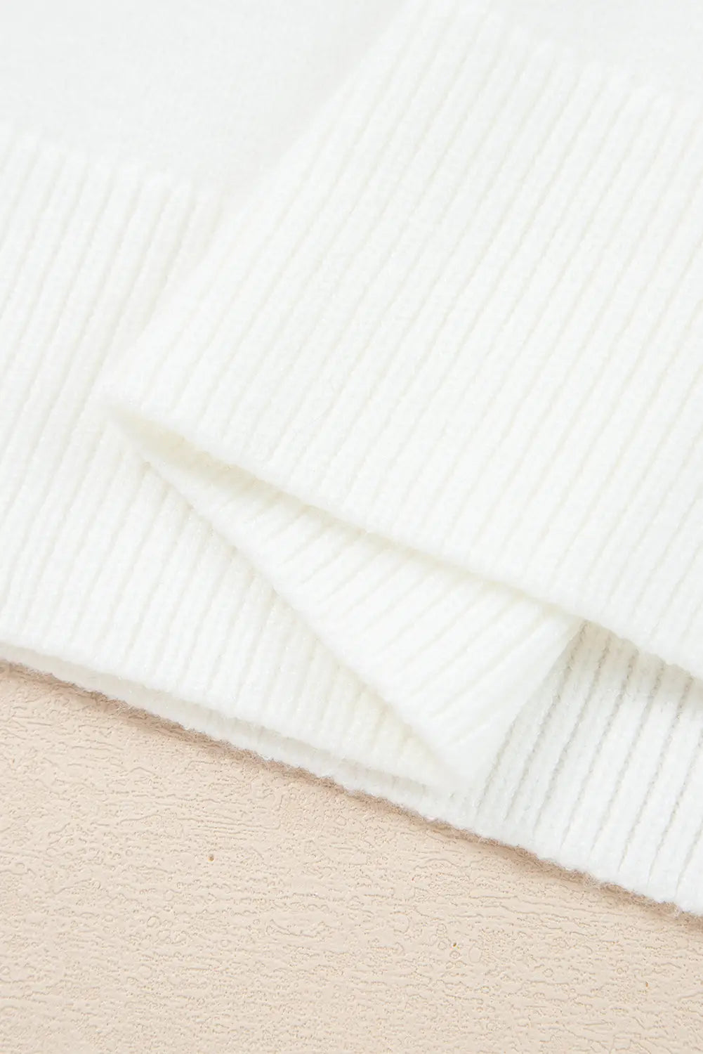 A close-up of folded white ribbed knit fabric, showing the soft texture and stitch pattern against a light beige background.