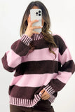 A woman takes a mirror selfie wearing a fuzzy knit sweater with wide horizontal stripes in dark brown and light pink, holding a white smartphone to block the camera.
