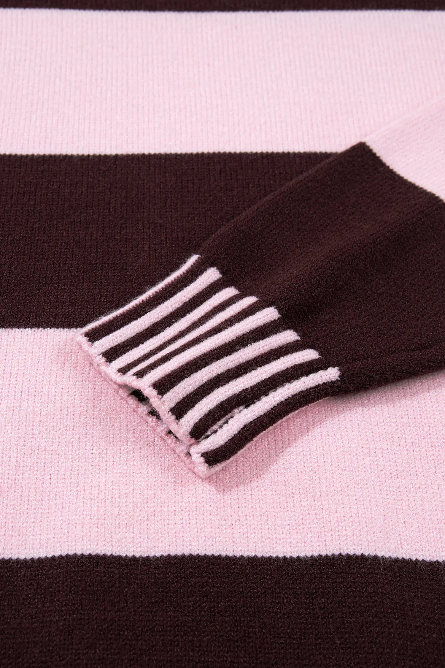 Close-up of a knit garment with wide horizontal stripes in light pink and very dark brown, showing a ribbed cuff with alternating pink and dark brown stripes.