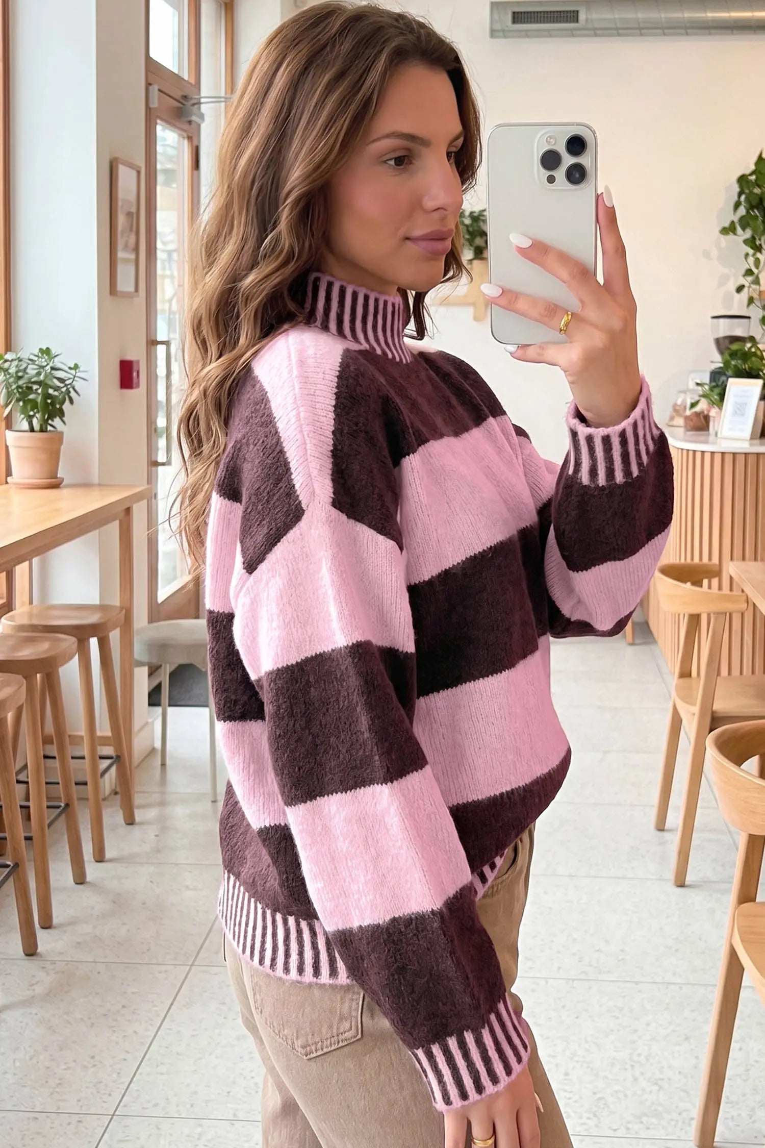 A woman takes a mirror selfie in a cafe while wearing a fuzzy knit mock-neck sweater with large pink and dark brown blocks.
