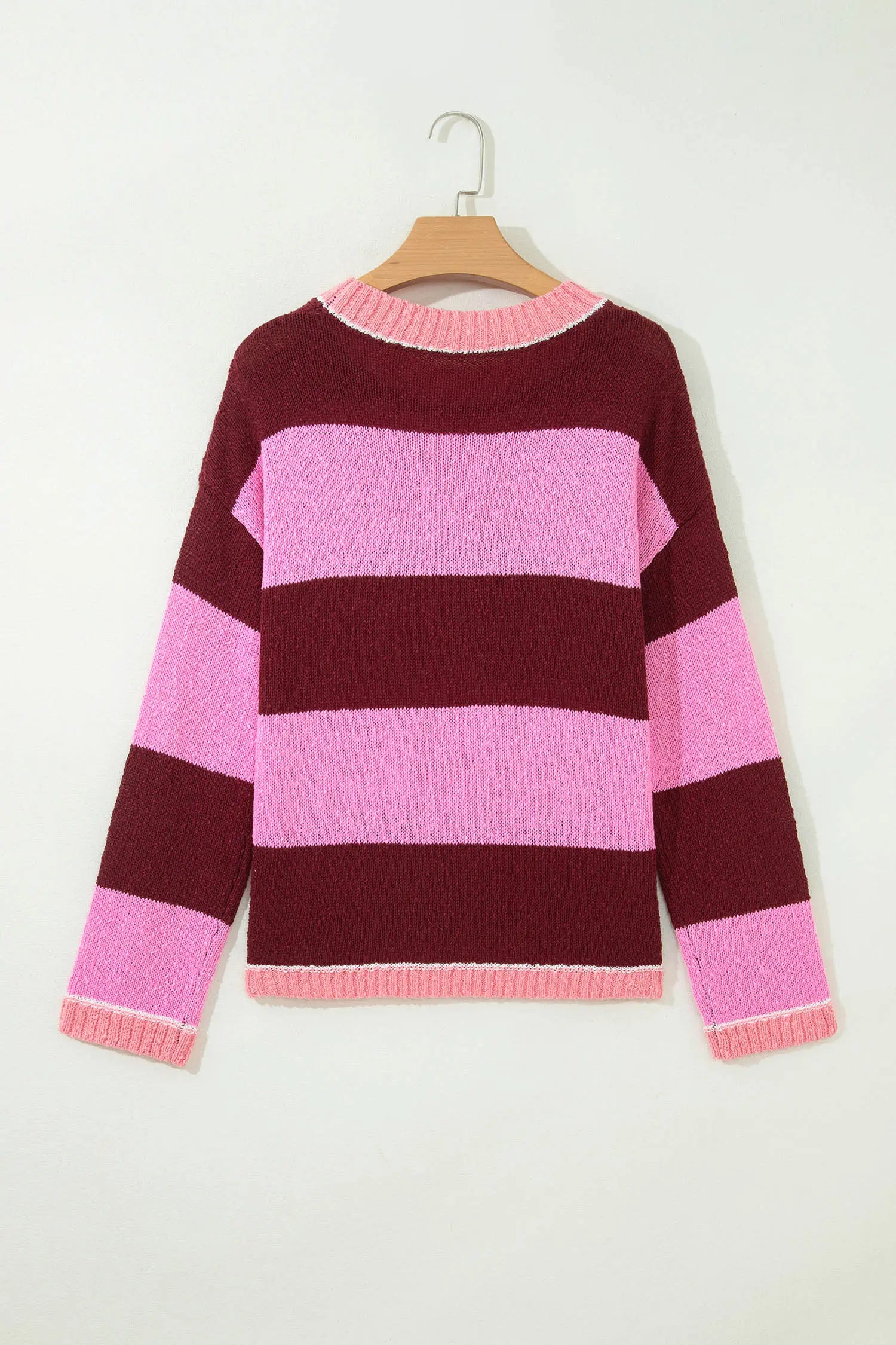 A pink and burgundy striped knit sweater hanging on a wooden hanger against a plain off-white wall.