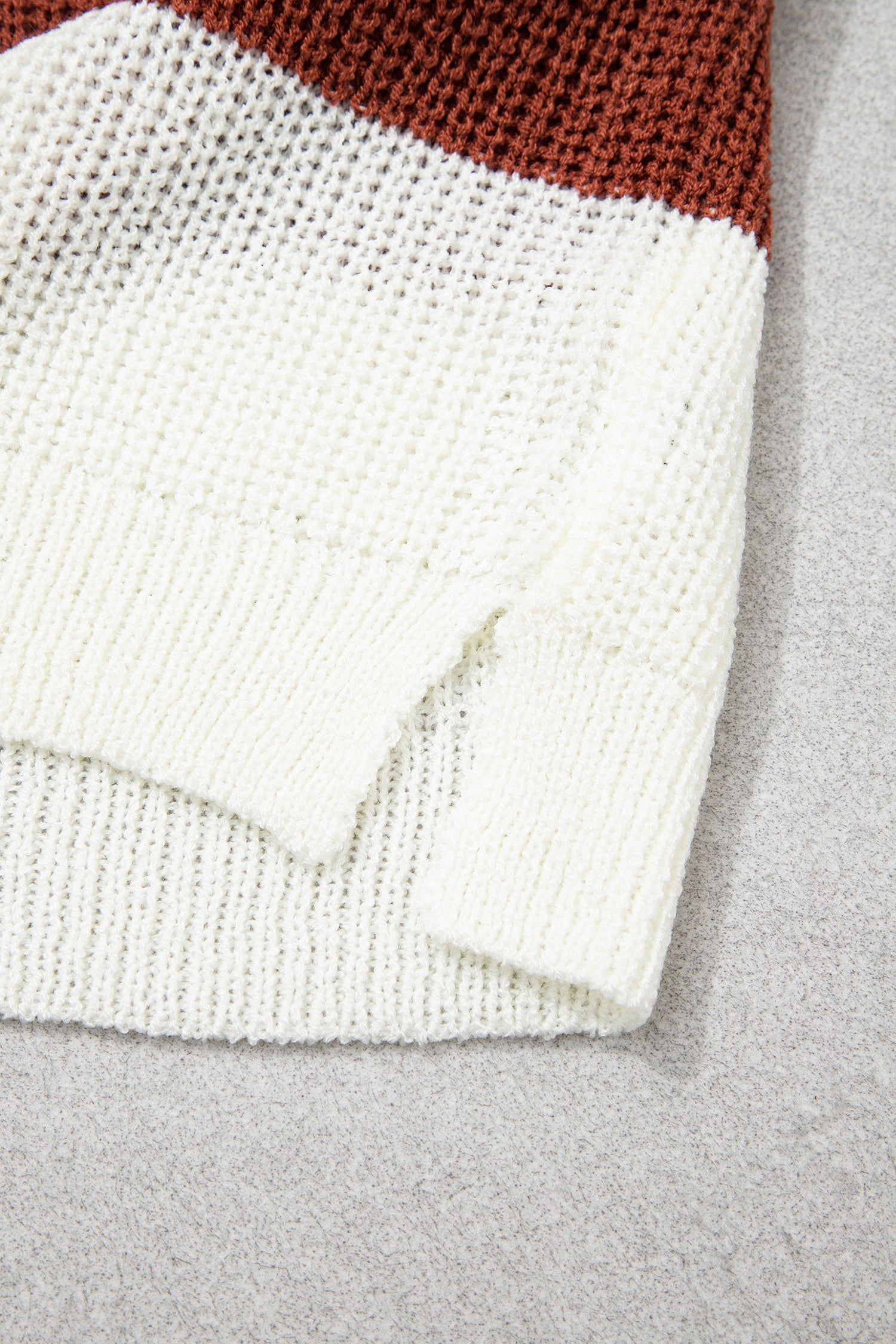 Close-up of a chunky knit beanie in off-white and rust brown, showing the ribbed cuff and knit texture on a gray background.