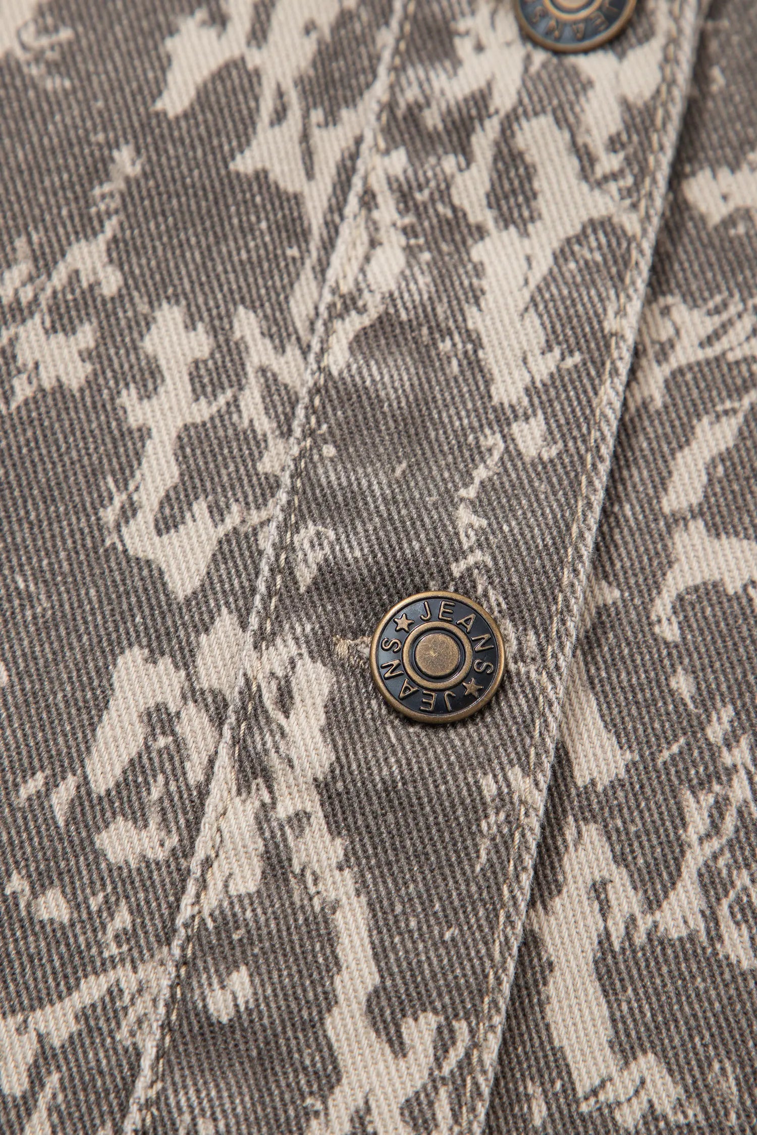 Close-up of gray and off-white camouflage denim jacket with a visible brass snap button.
