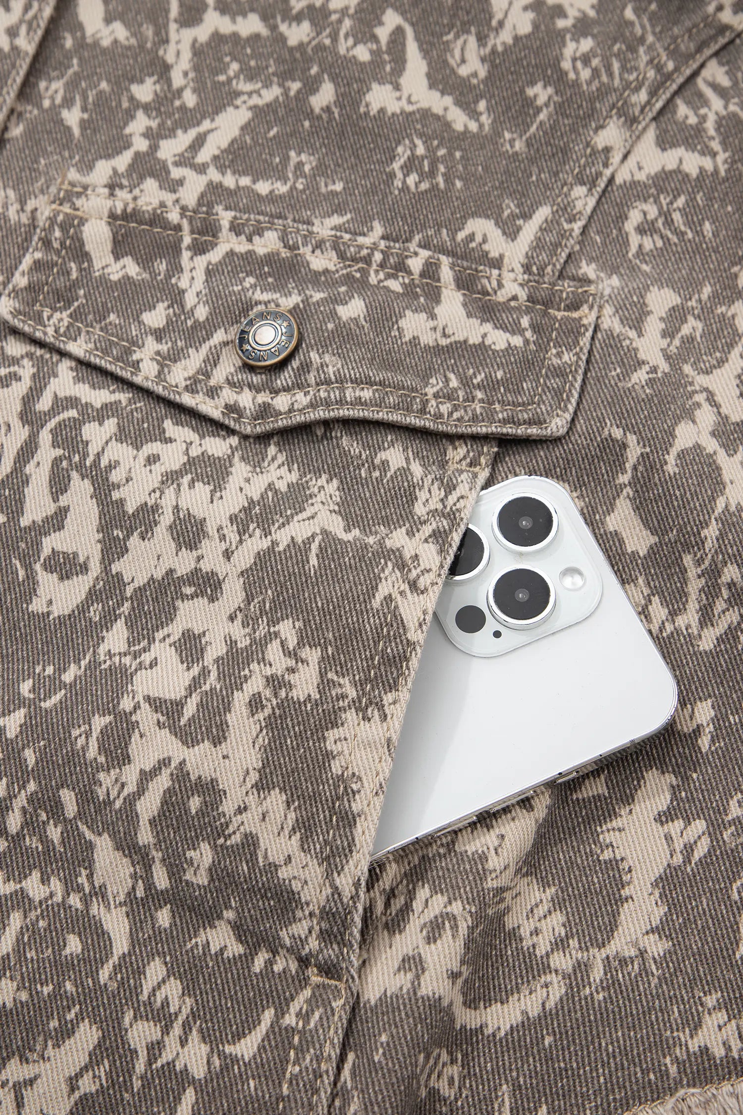 Close-up of brown-beige camouflage canvas jacket with buttoned chest pocket and white smartphone in side pocket.