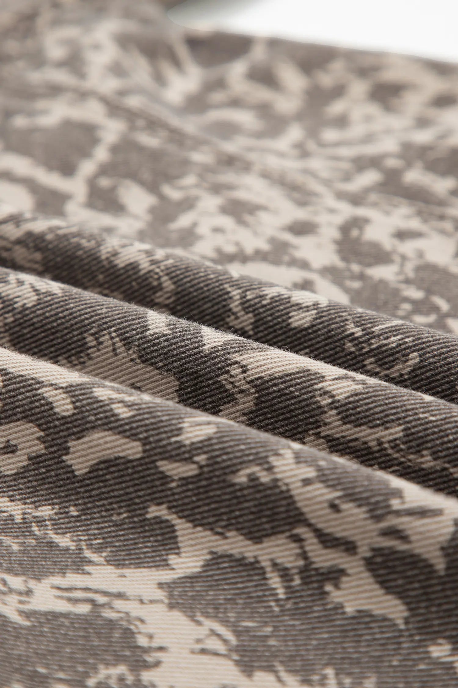 A close-up of draped fabric with a dark gray and beige abstract camouflage pattern.