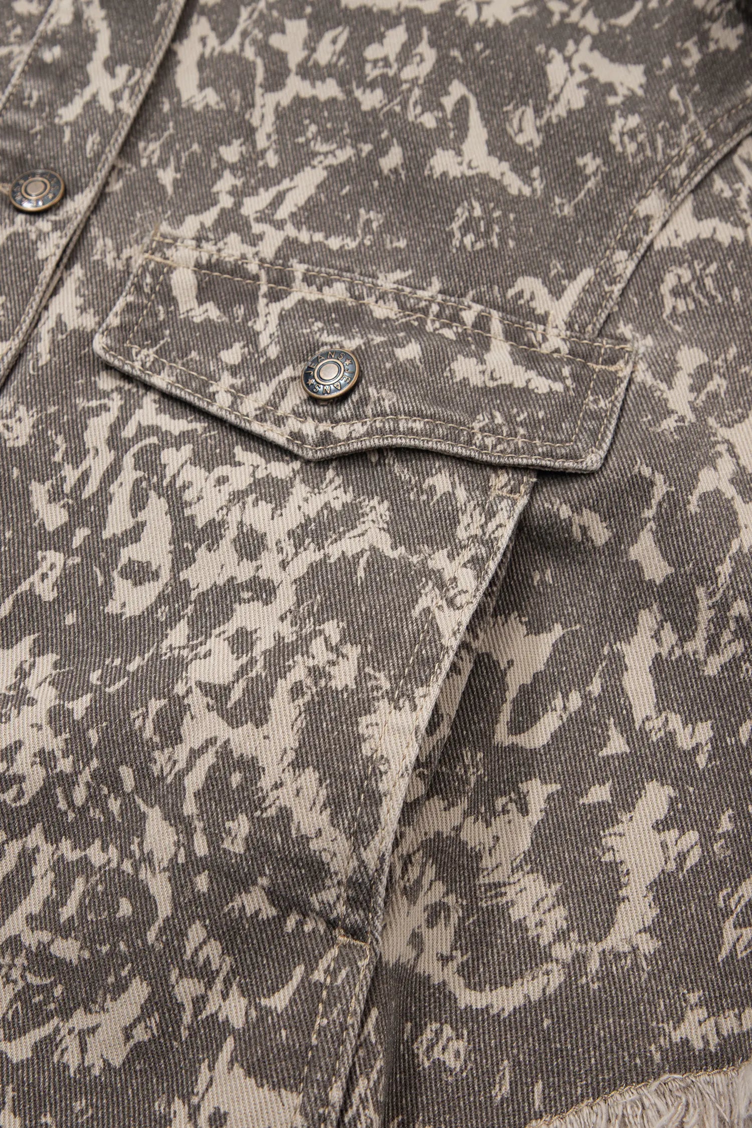 Close-up of textured gray and beige canvas shirt with chest pocket and metal snap buttons.