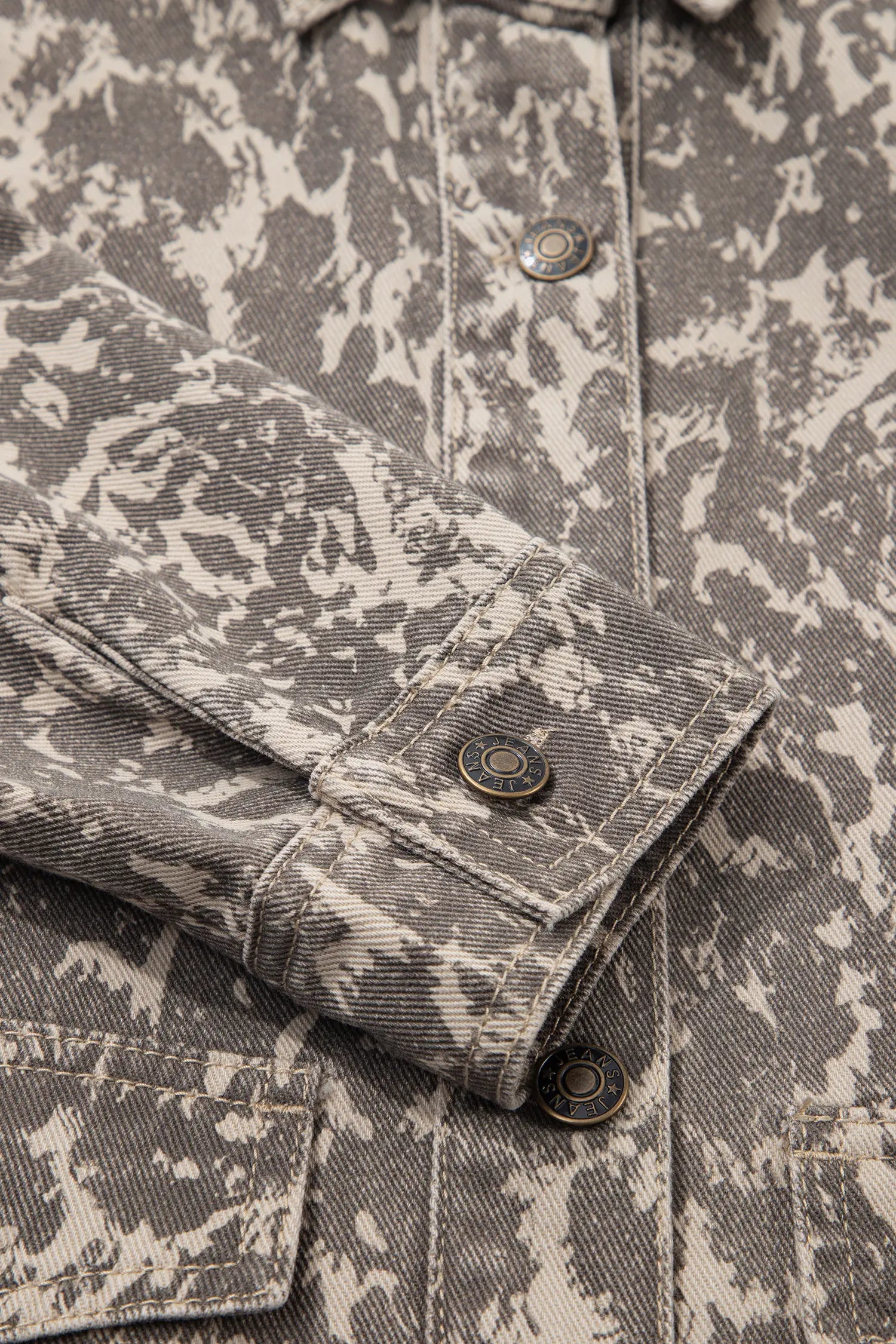 Close-up of gray and off-white camouflage denim shirt jacket with textured fabric, buttons, and pocket stitching.