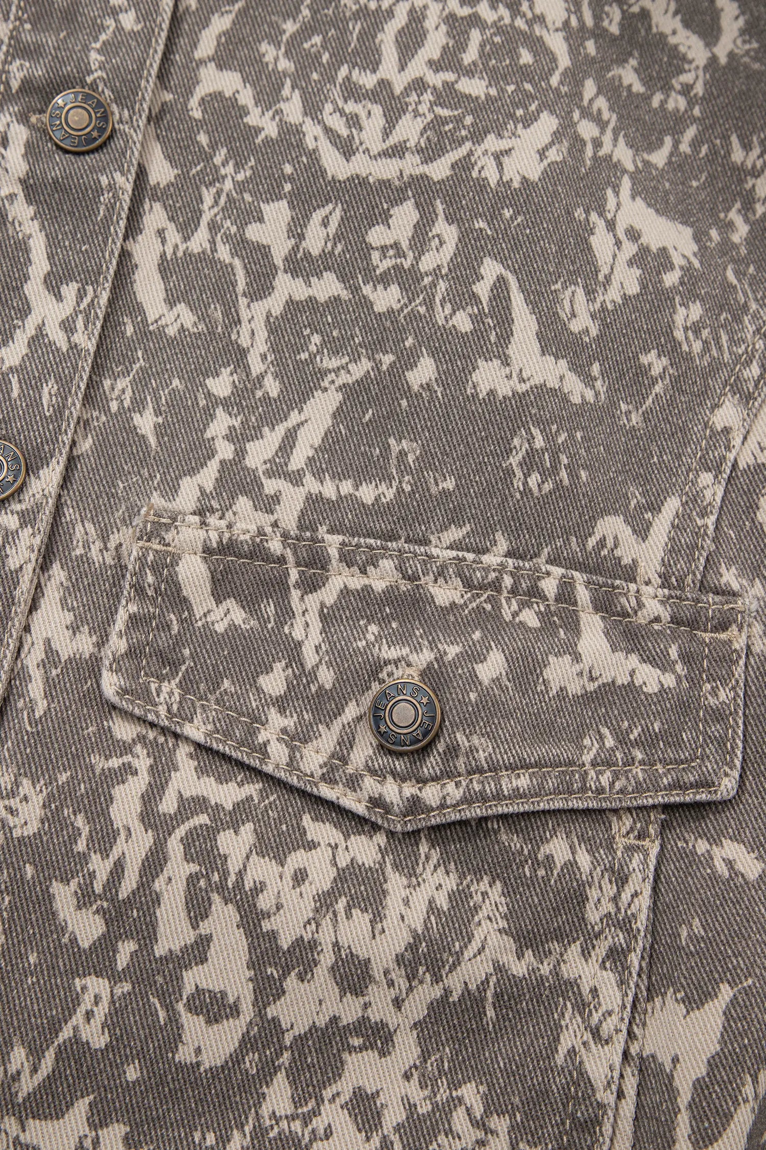 Close-up of gray and off-white camouflage denim jacket with buttoned chest pocket and snap buttons.