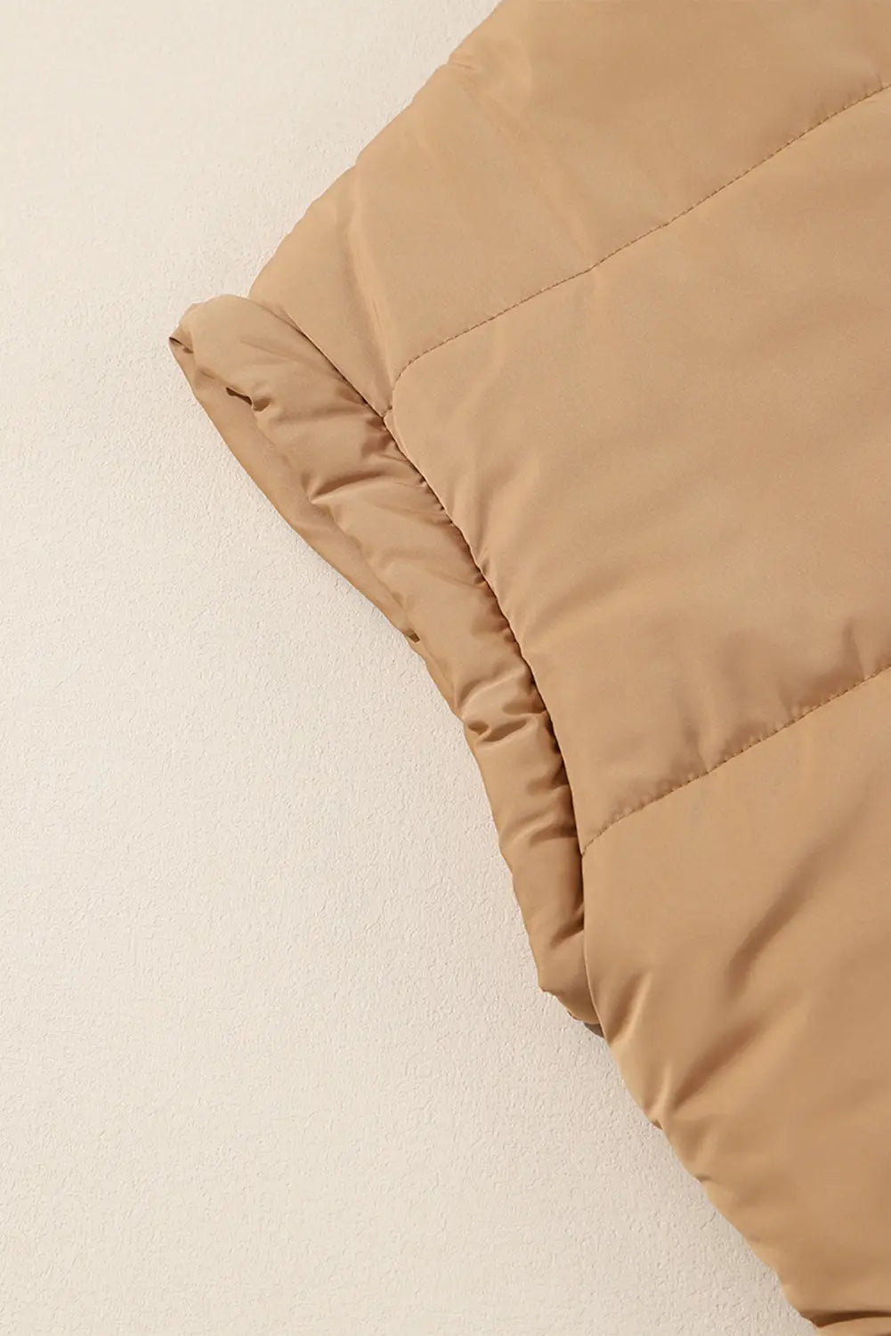A close-up of a tan quilted puffer sleeve or vest section laid against a plain off-white background.
