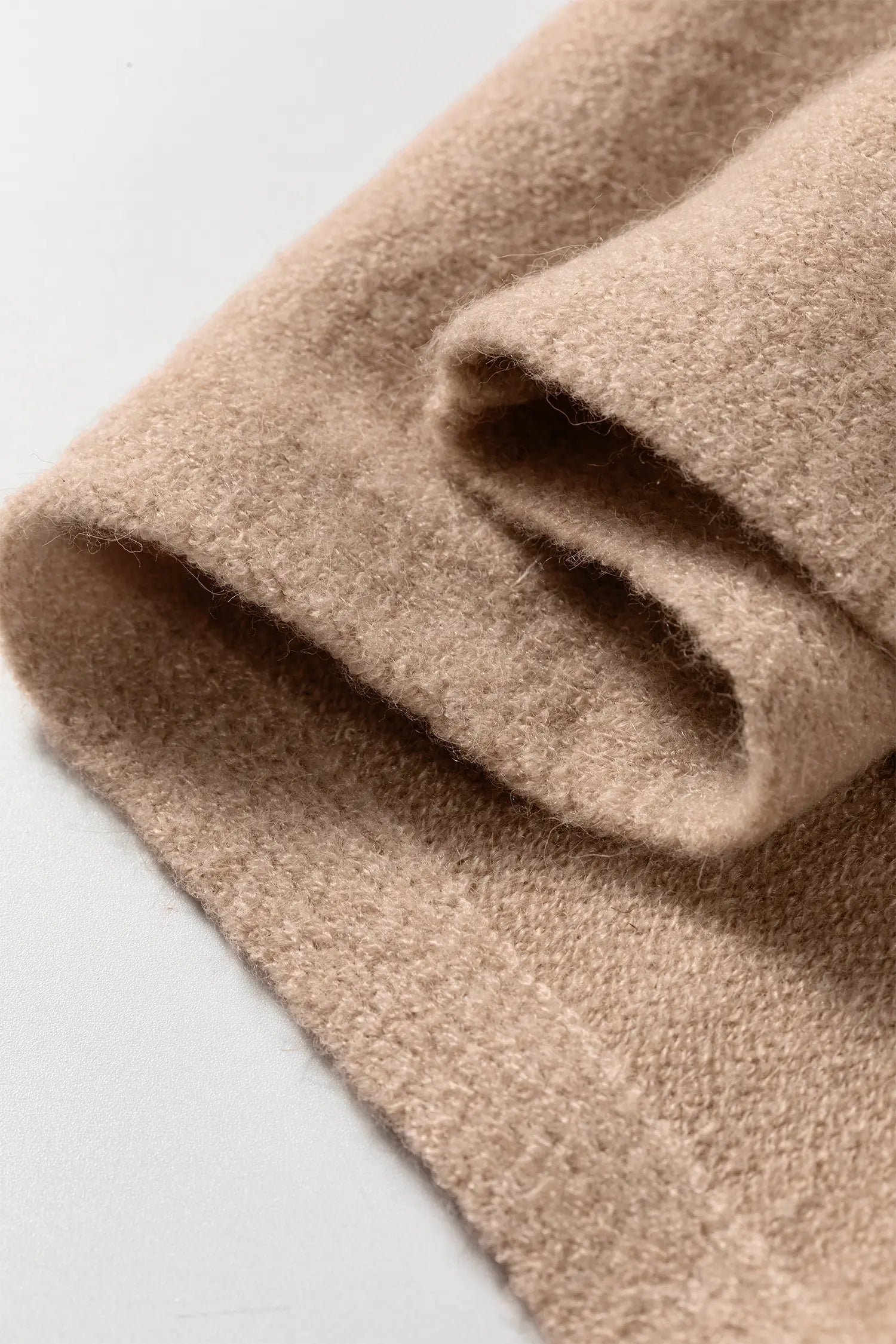 A close-up of folded beige fabric with a soft, textured surface on a light gray background.