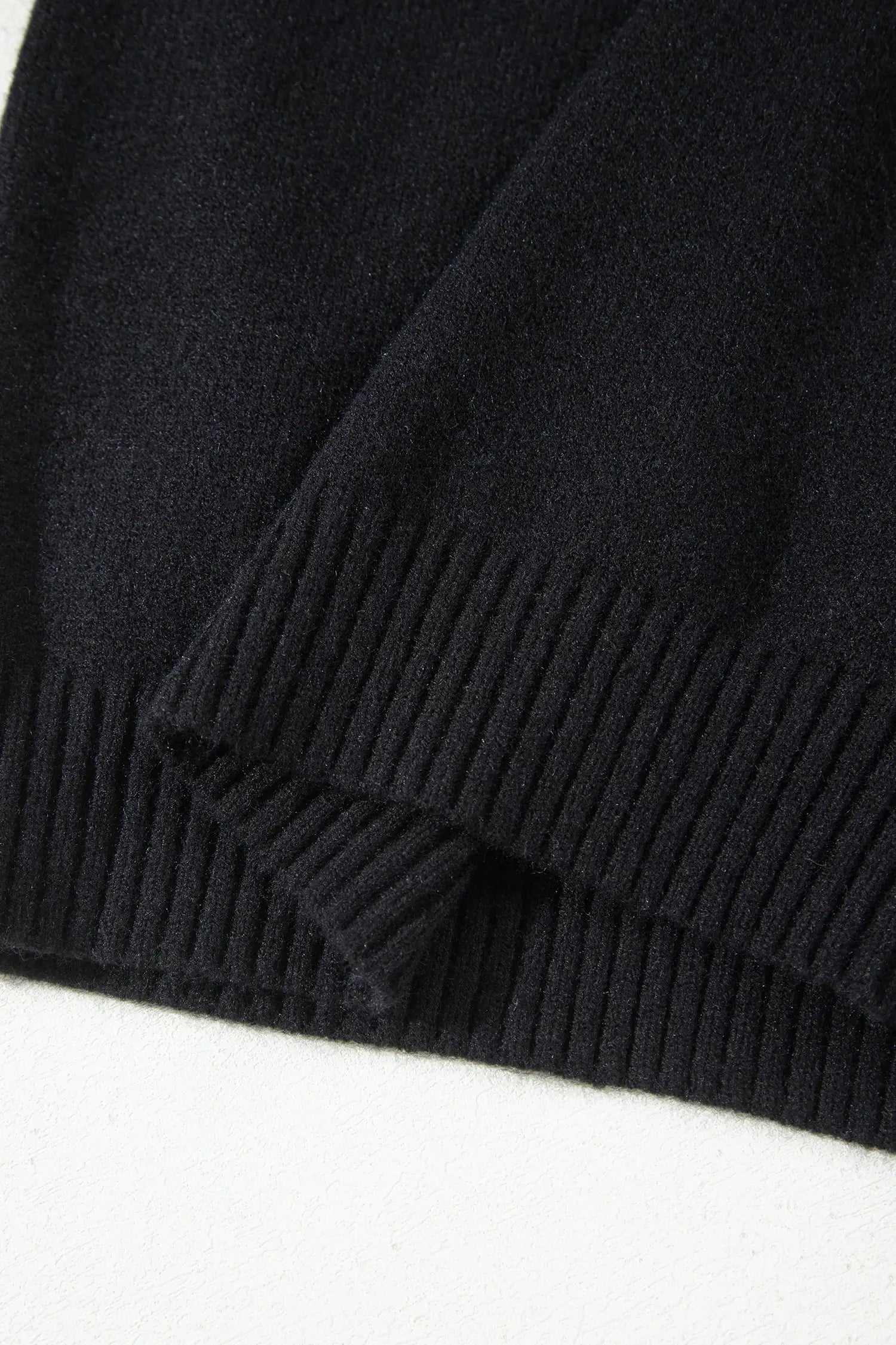 Close-up of a black ribbed knit fabric, showing the texture and folded edges of the material against a white background.