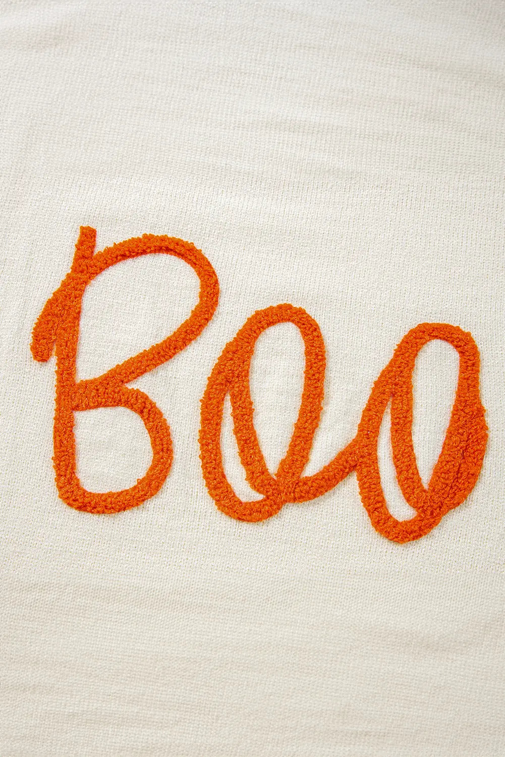 A close-up of a textured cream-colored fabric with the word 'Boo' embroidered in bright orange cursive script.